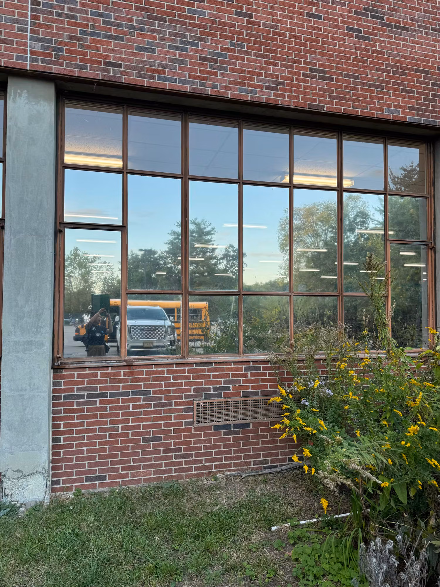 Large multi-pane window on a brick building with darkened reflective solar film mirroring the parking lot.