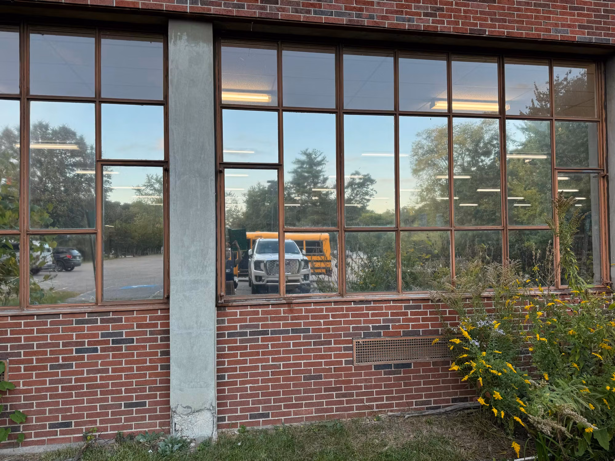 Bank of multi-pane school windows with reflective film showing the parking lot and a school bus outside.
