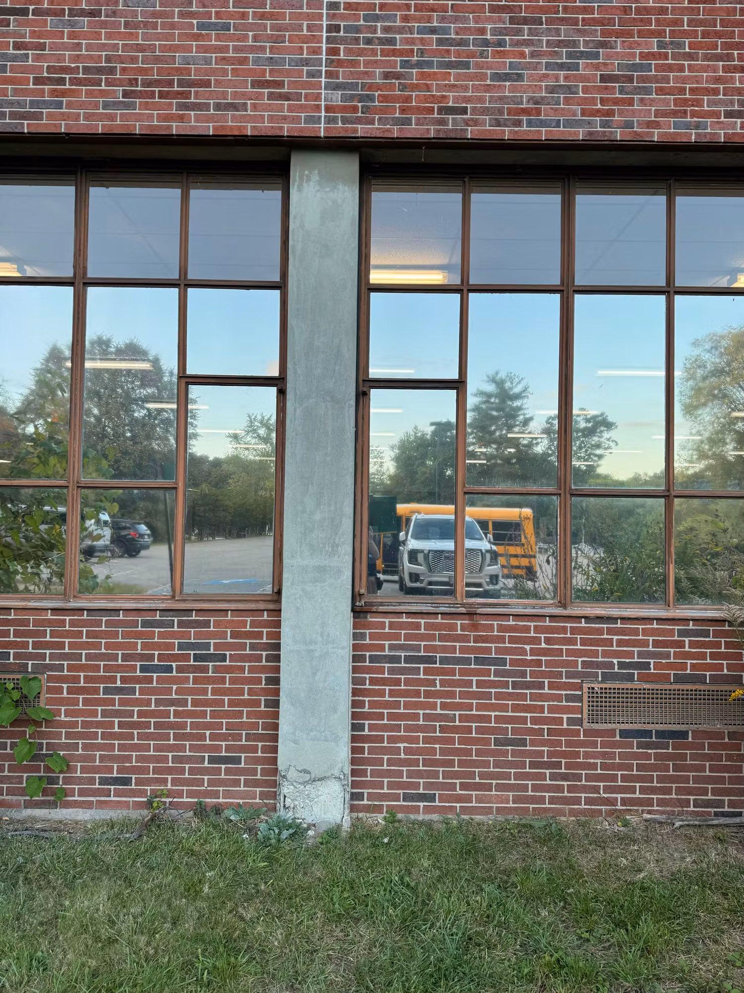Paired multi-pane school windows in brick with reflective film mirroring trees and a parked work truck.
