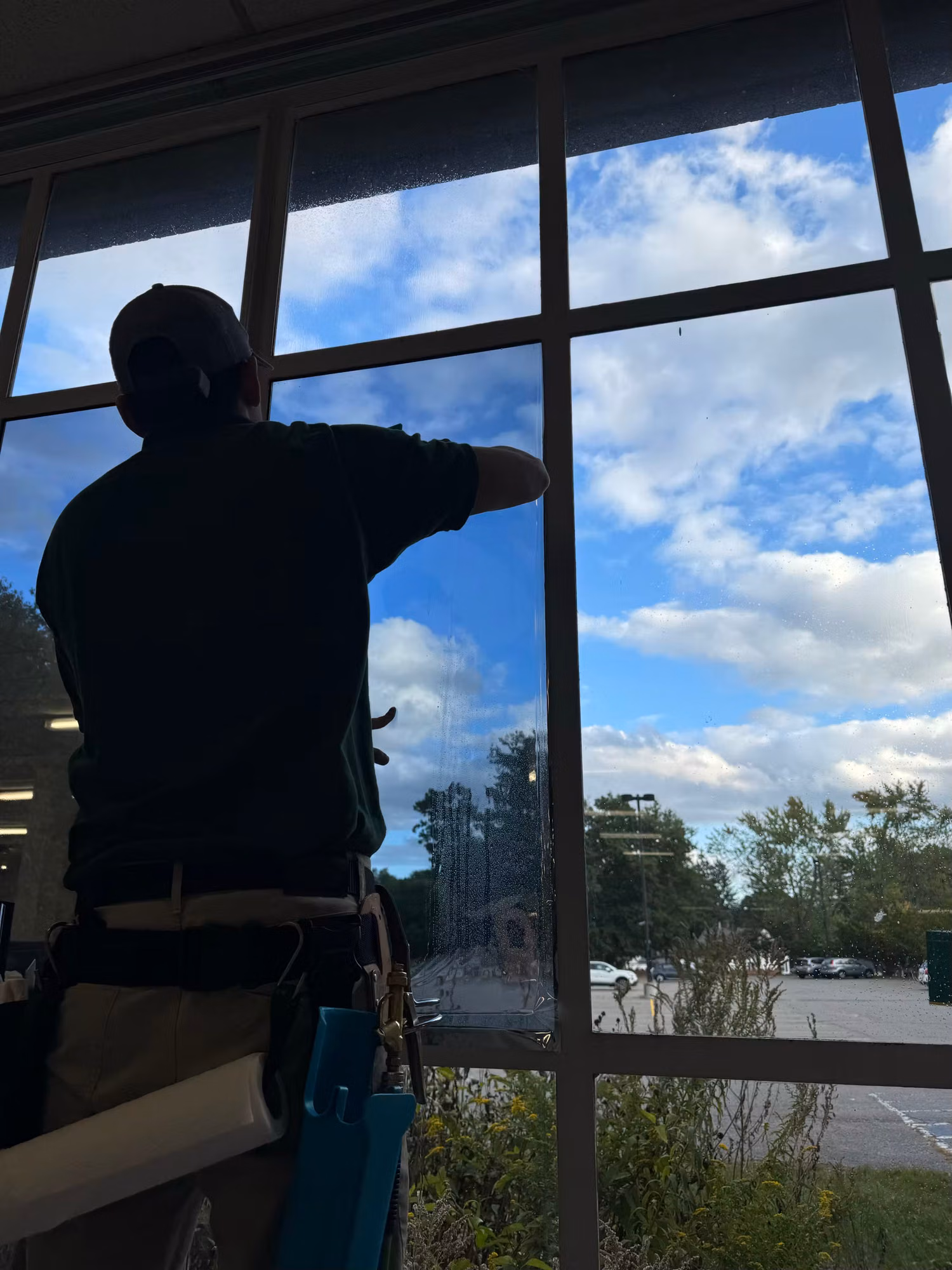 Technician smoothing freshly installed film across a tall multi-pane commercial window from the interior.
