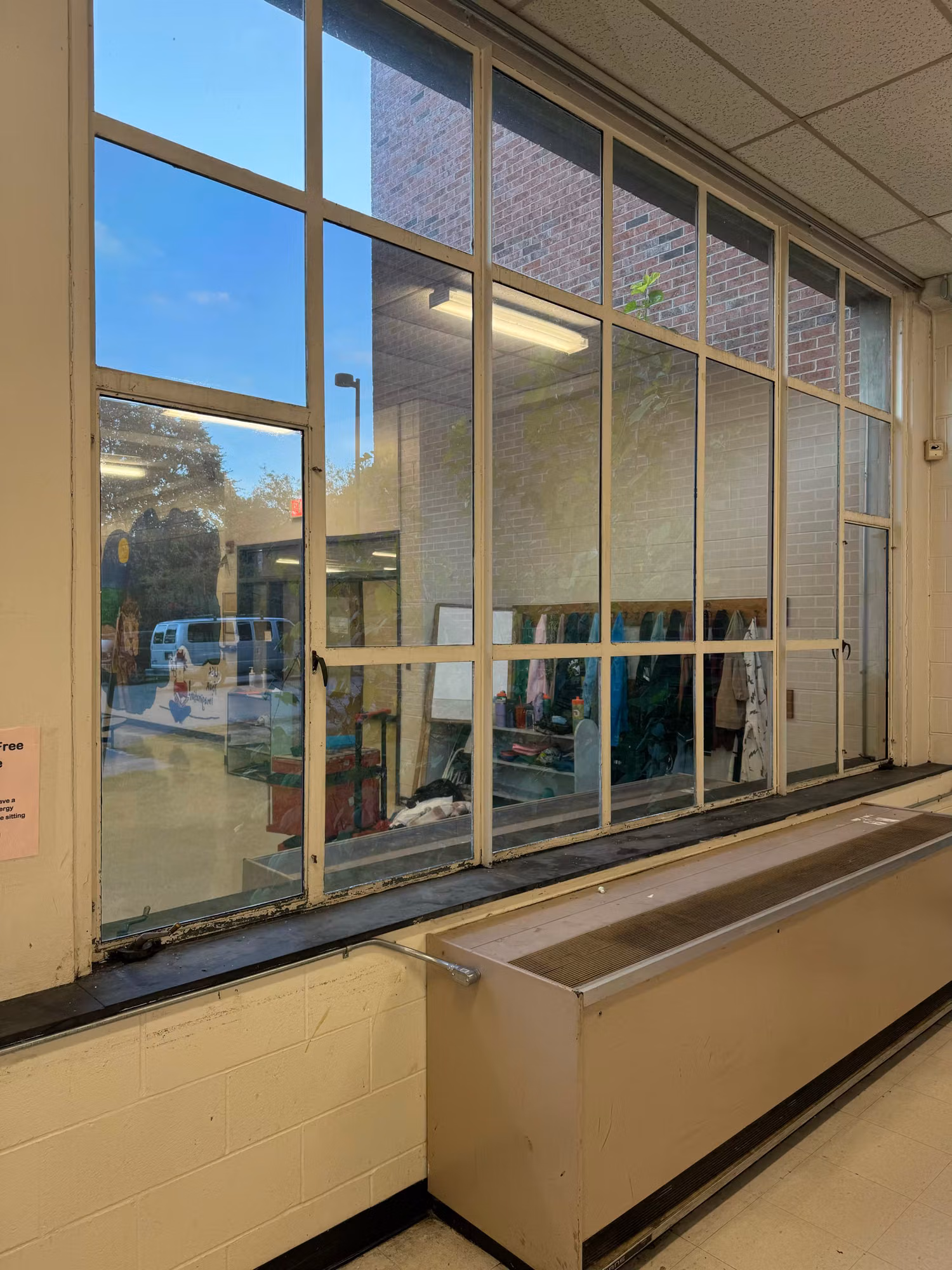 Tall multi-pane interior window wall with solar film separating a corridor from an adjoining school room.