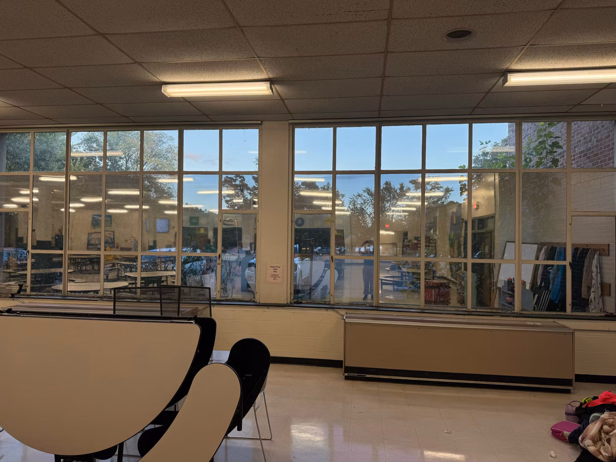Wide school room interior with a full-height window wall carrying solar film and round tables in the foreground.