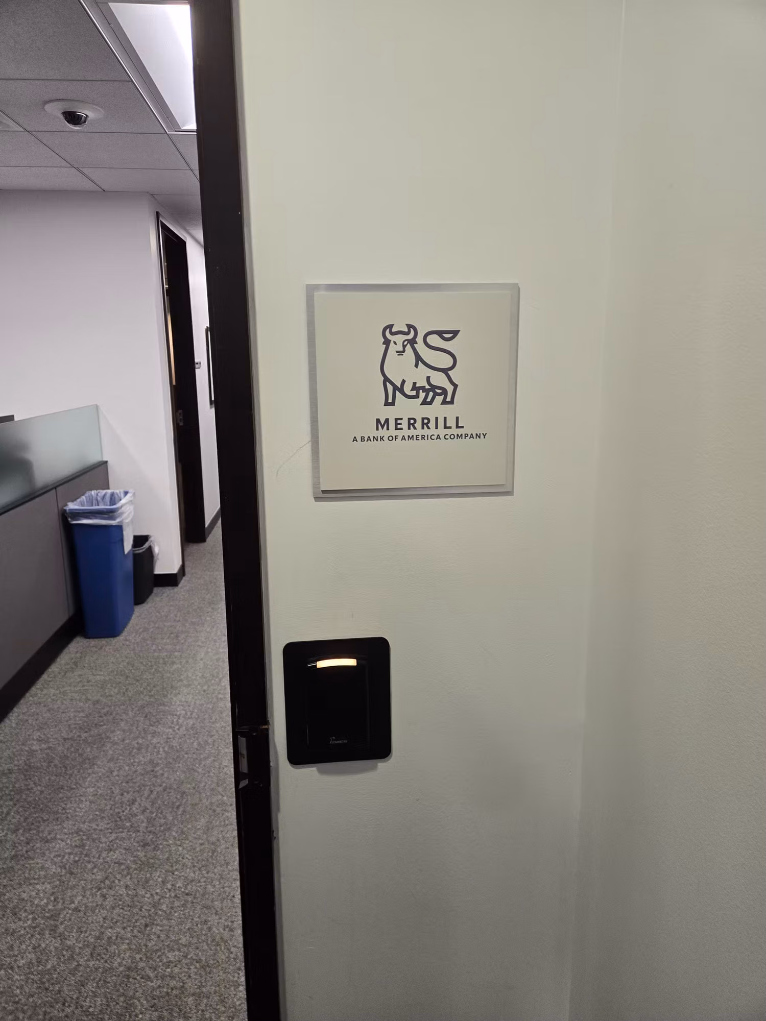 Framed office signage panel mounted on an interior corridor wall beside a card-access reader.