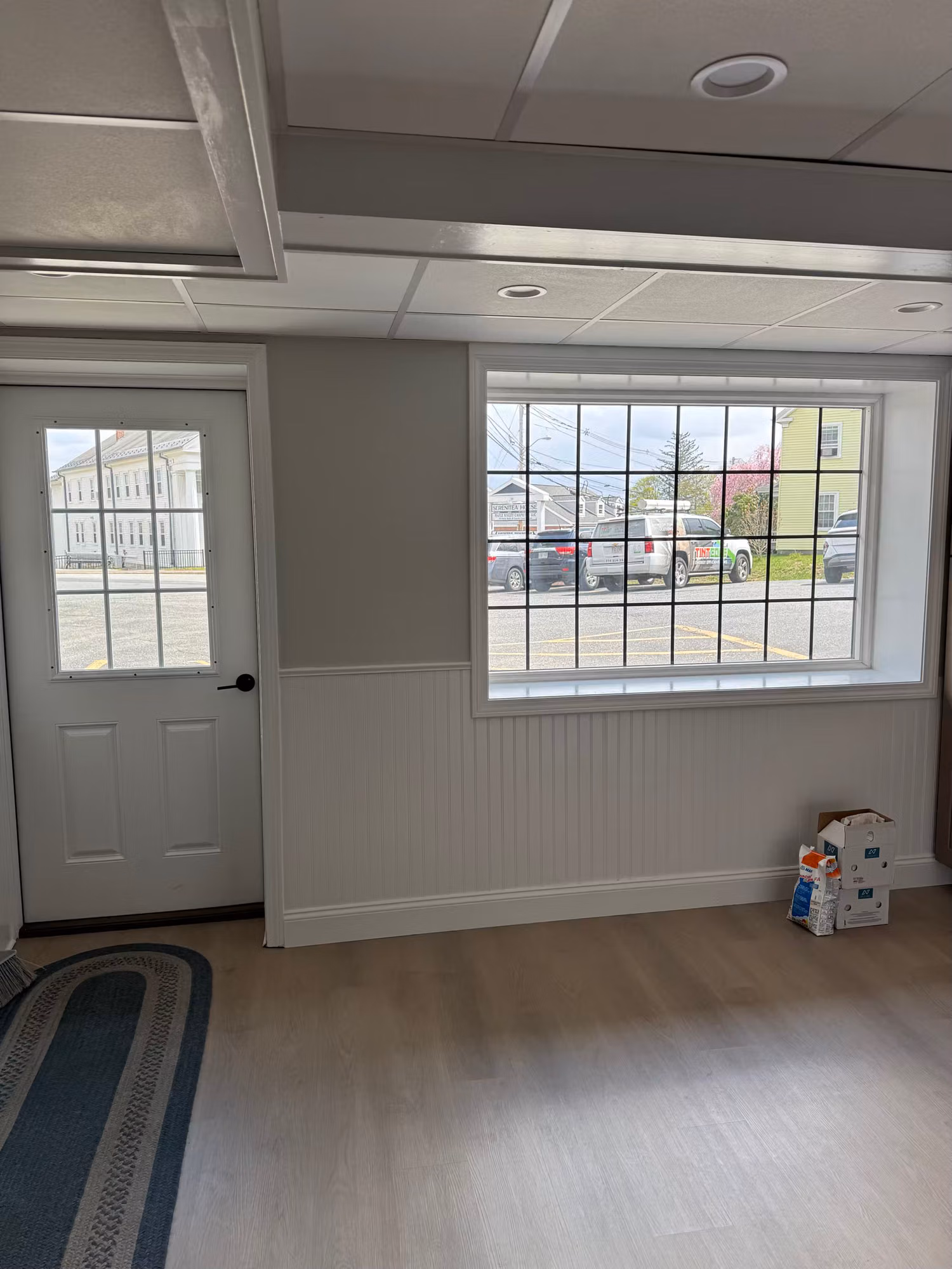 Interior commercial room with a large gridded picture window and a white entry door overlooking a parking lot.