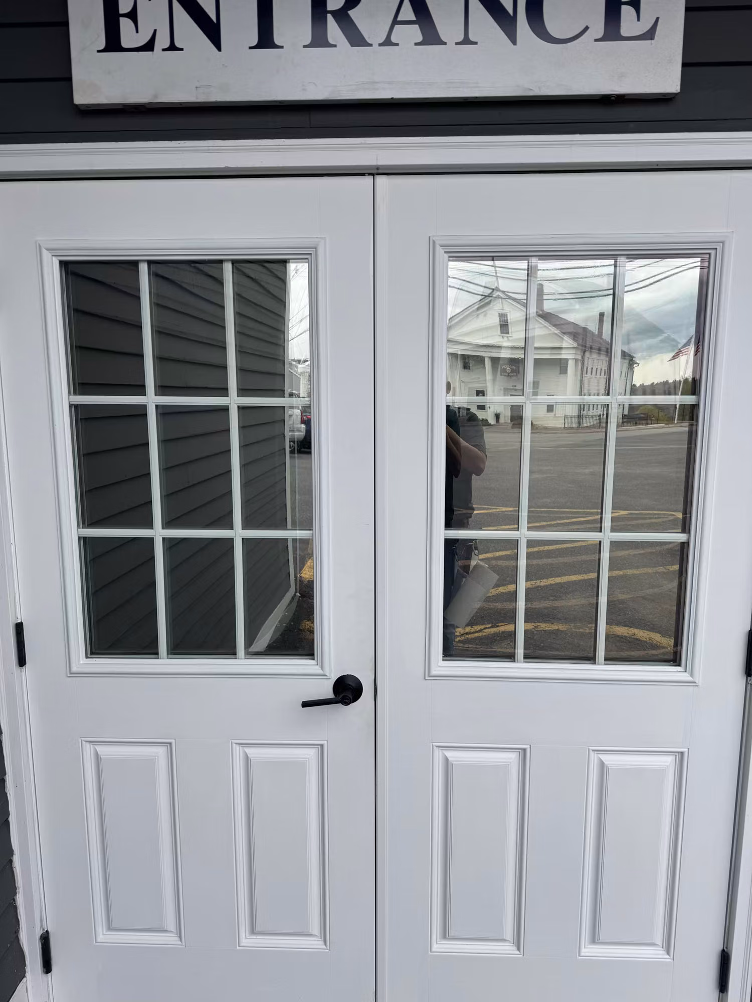 White double entry doors with gridded glass lights under an entrance sign, the door glass darkened by applied window film.