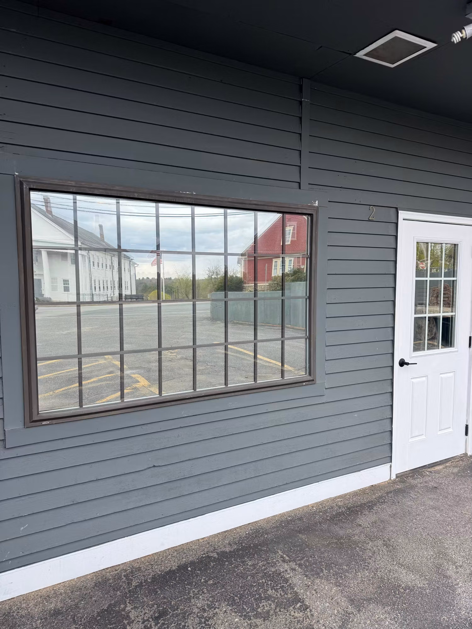 Exterior wall of a commercial building showing a gridded picture window and a glass entry door with film applied to the glass.