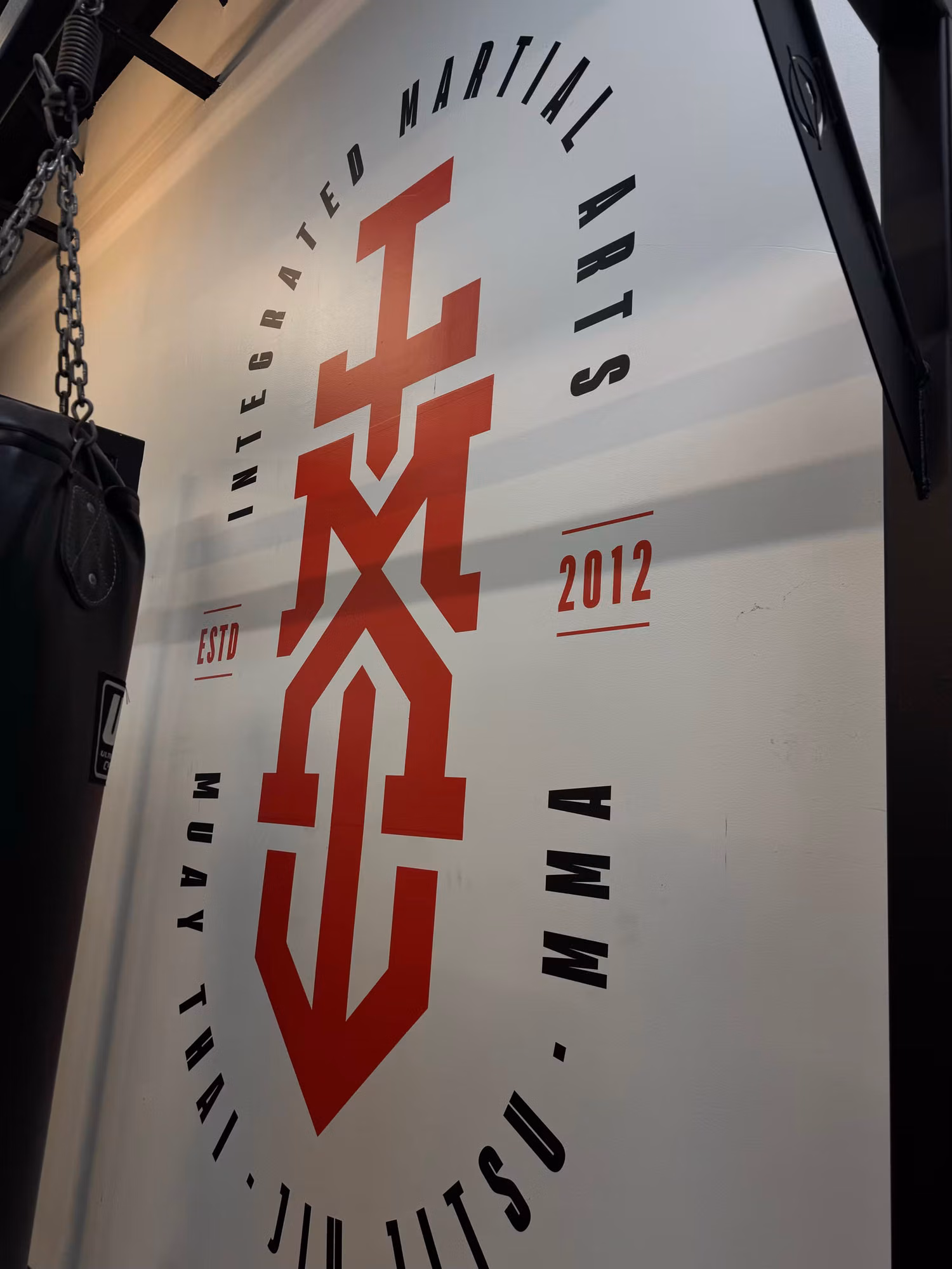 Angled view of a red and black cut-vinyl logo decal applied to a martial arts gym wall.