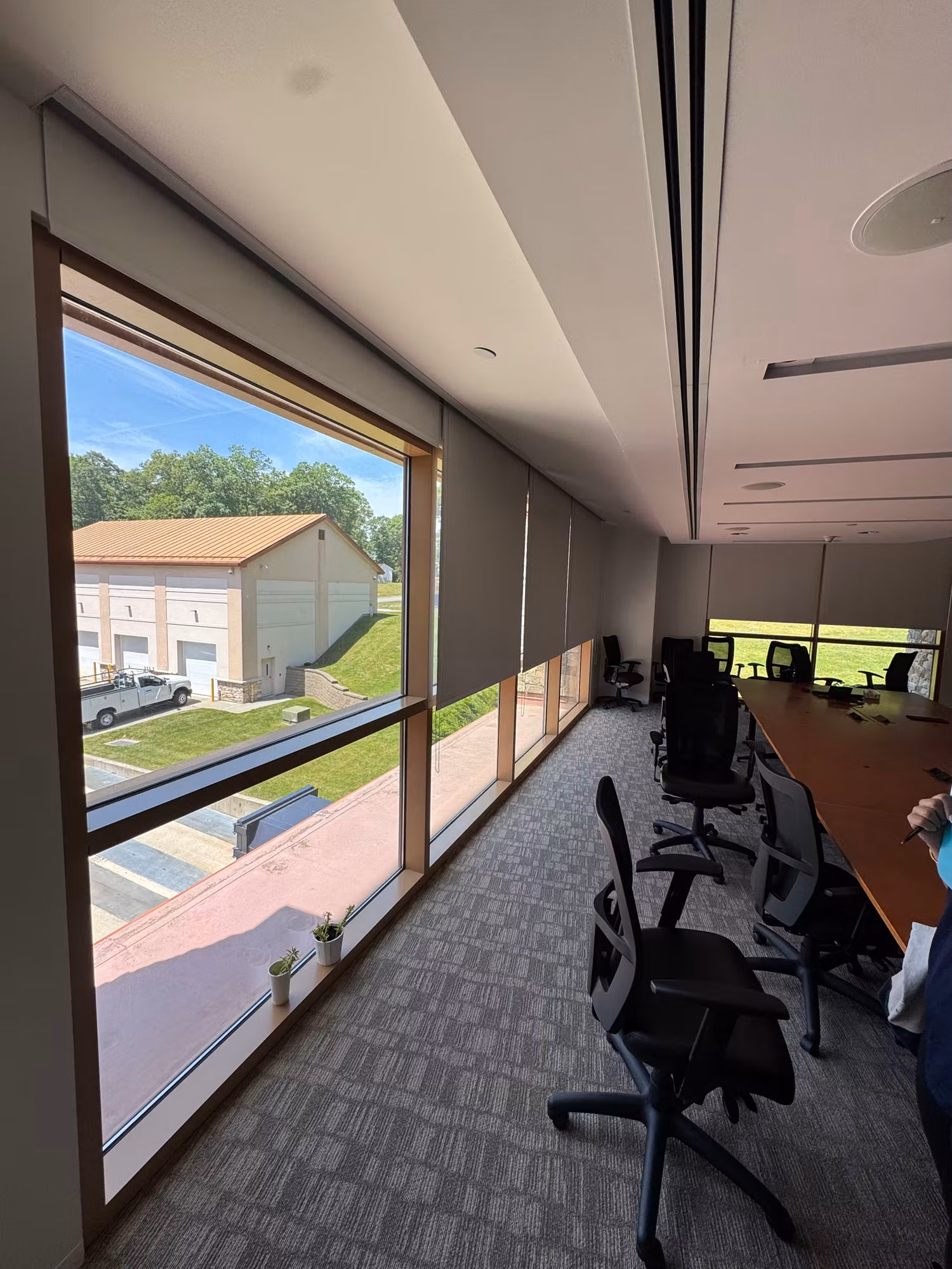 Long office room with a row of ribbon windows fitted with light-diffusing solar shades beside table seating.