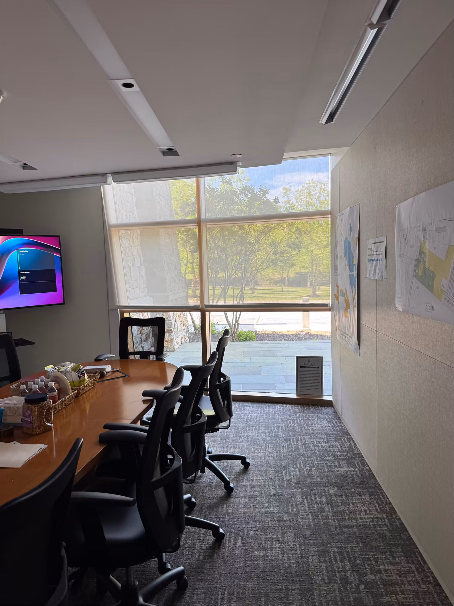 Conference room window with a solar screen shade softening daylight over a meeting table and wall display.