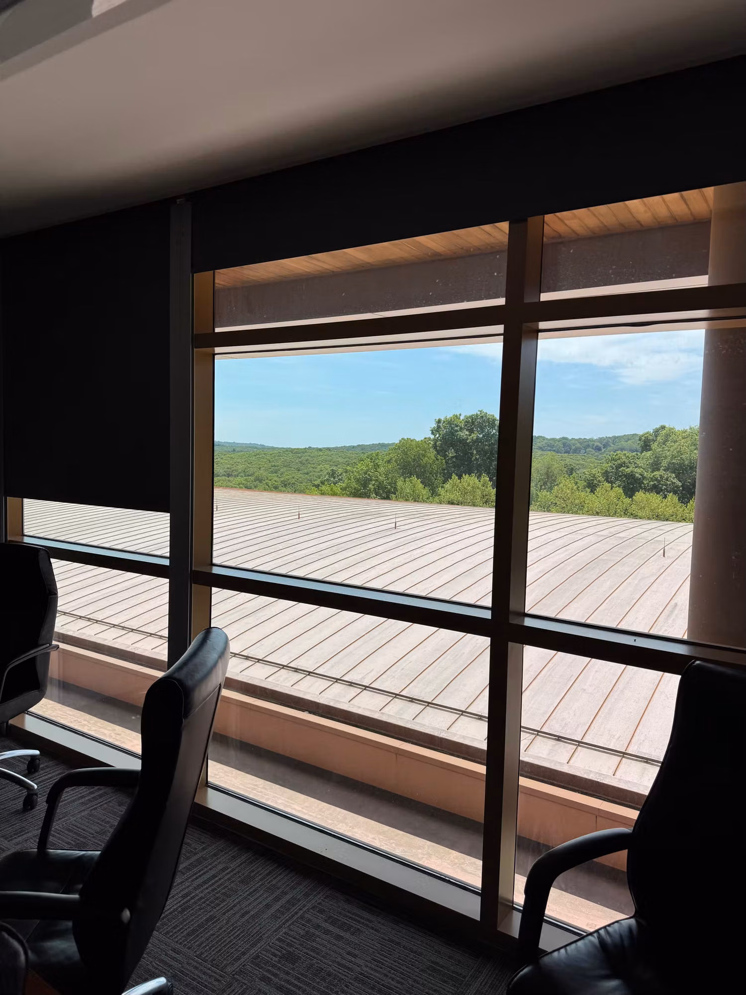 Conference room with large windows and roller solar shades framing a view of rooftops and green hillside.