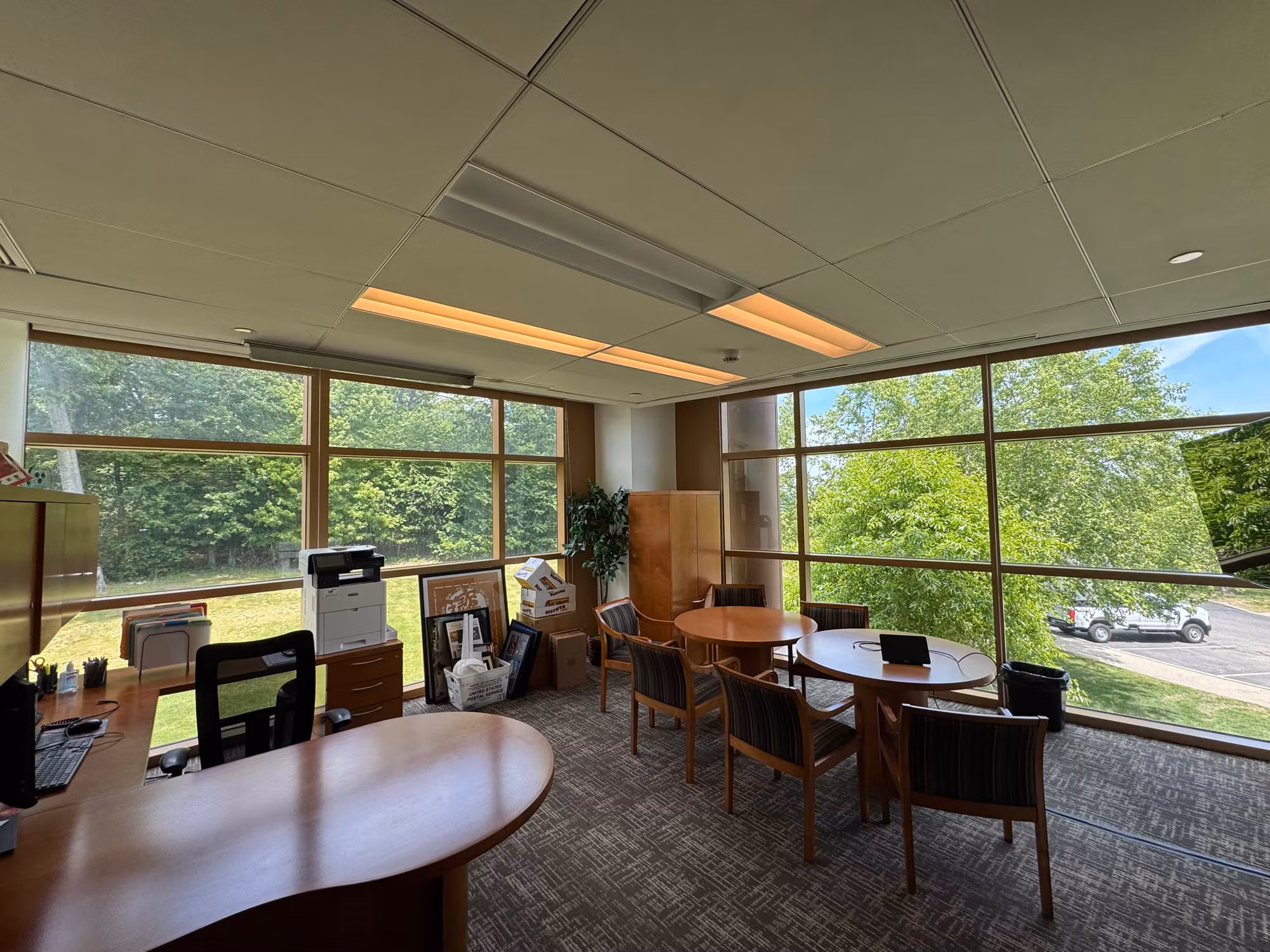 Corner office with wraparound windows and solar screen shades cutting glare over a meeting table.