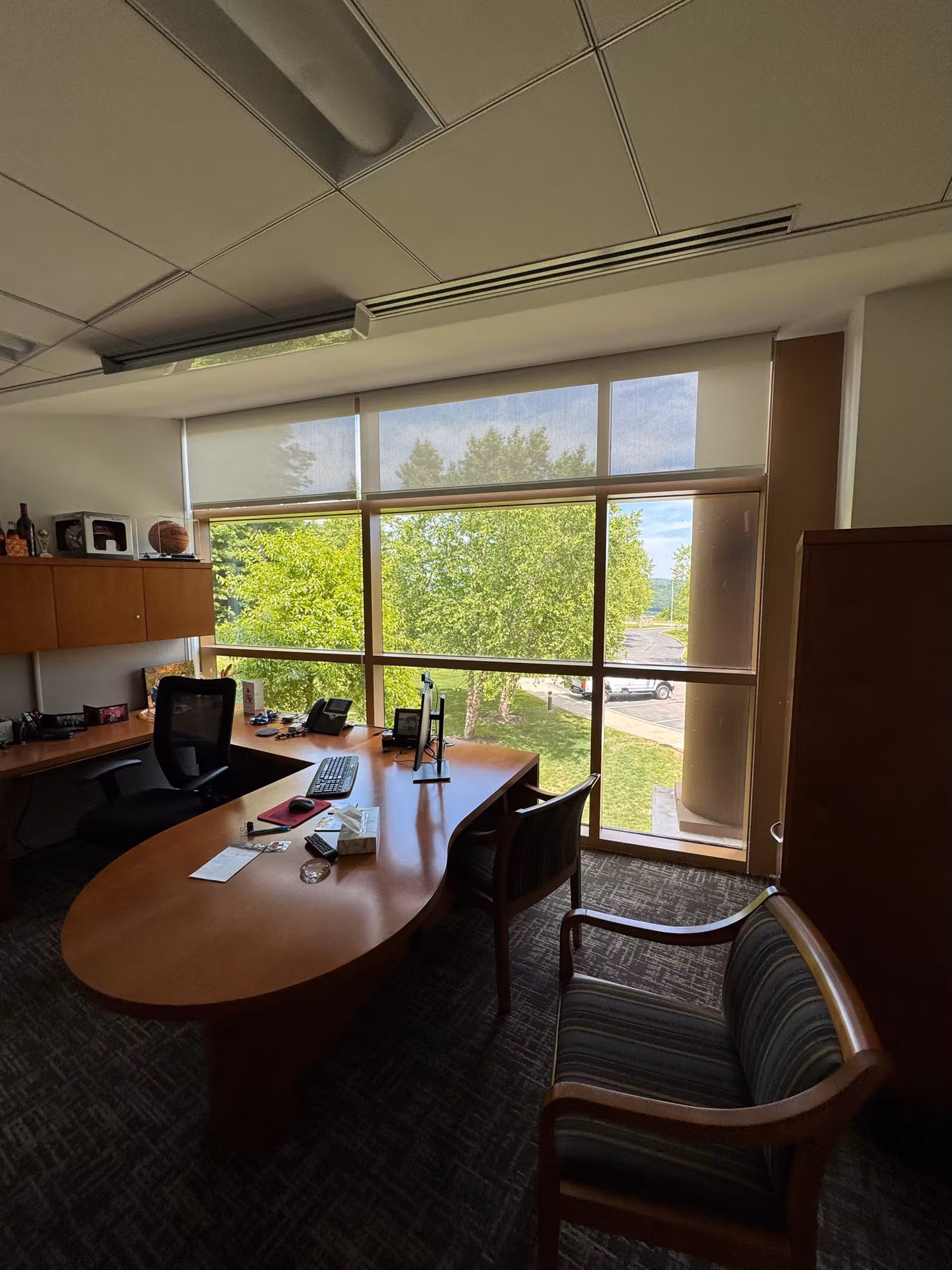 Executive office desk beside a large window with a partly raised solar shade and a green outdoor view.