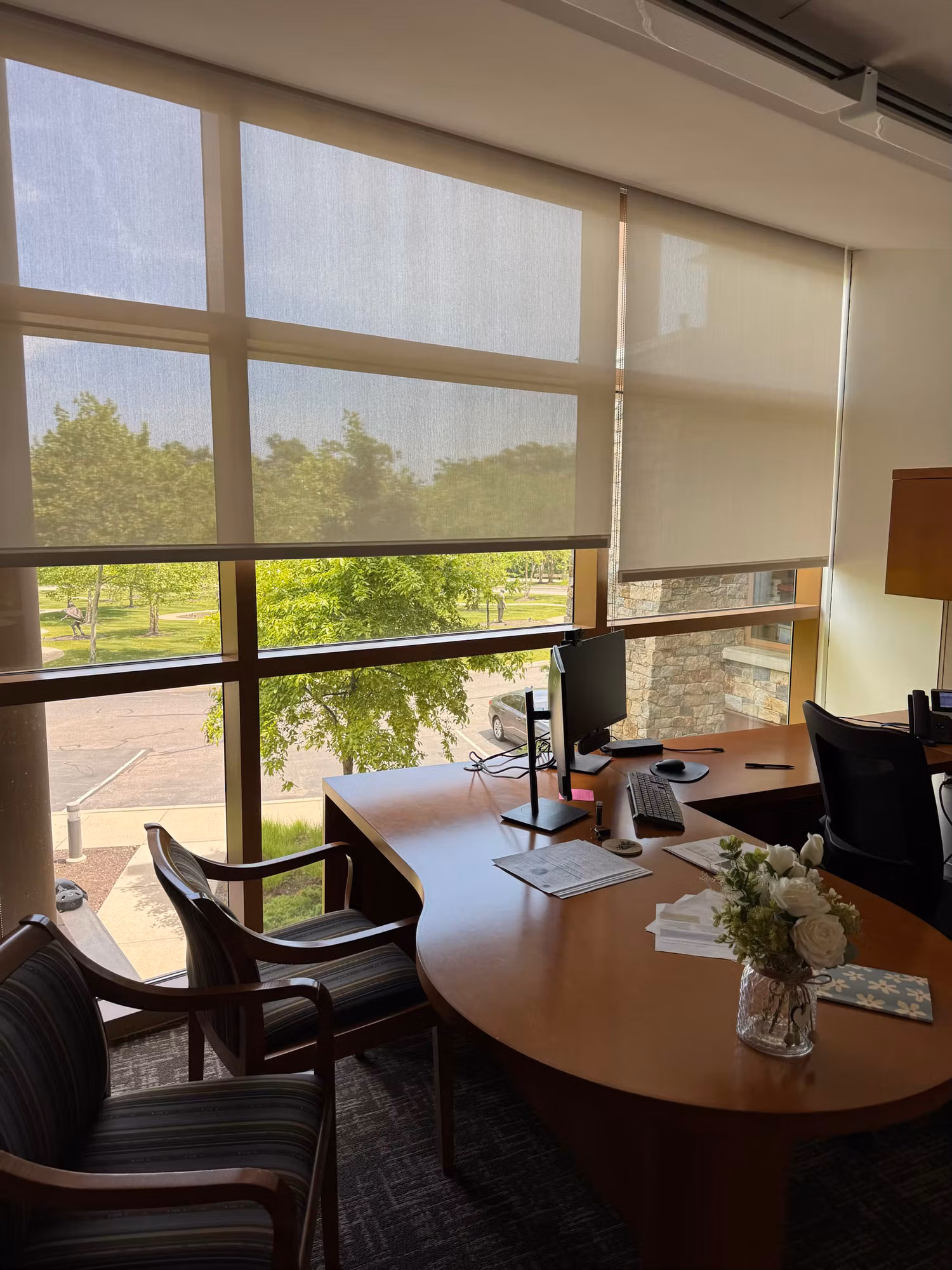 Office corner with floor-to-ceiling windows and light-diffusing solar shades over a desk and seating.