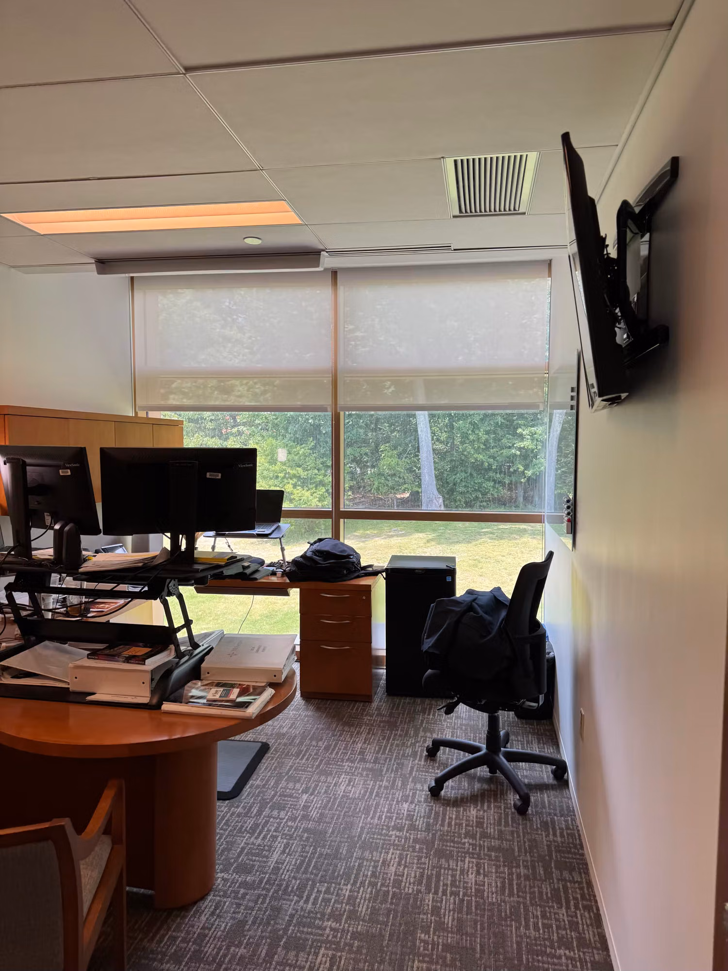 Office workstation with monitors beside a window fitted with a light-filtering solar shade.