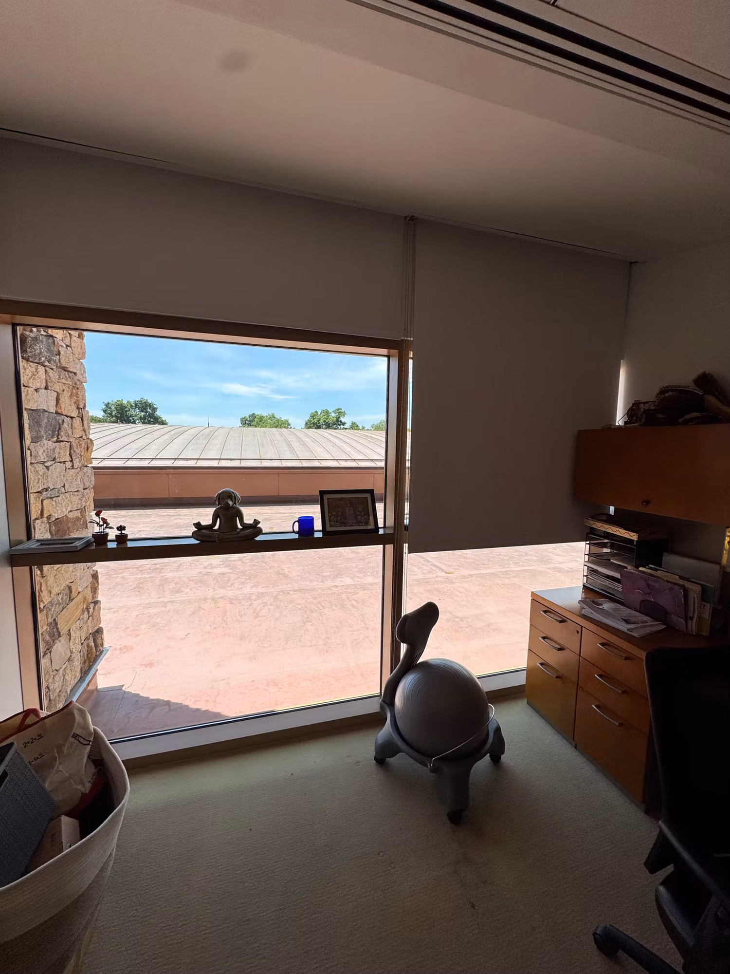 Private office with a large picture window overlooking a courtyard and a solar roller shade raised above the glass.