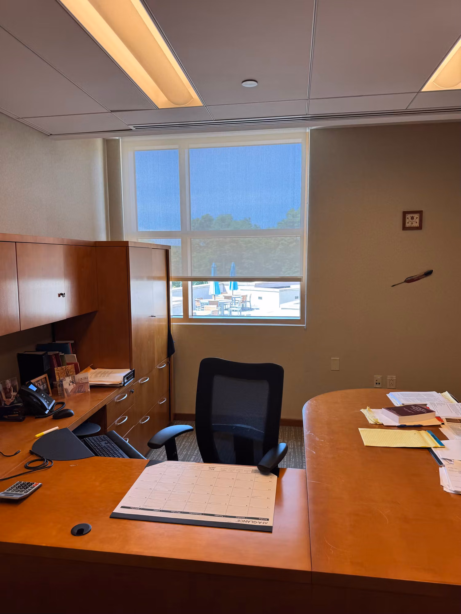 Private office with a wood desk and a window treated with solar control film overlooking a parking area.