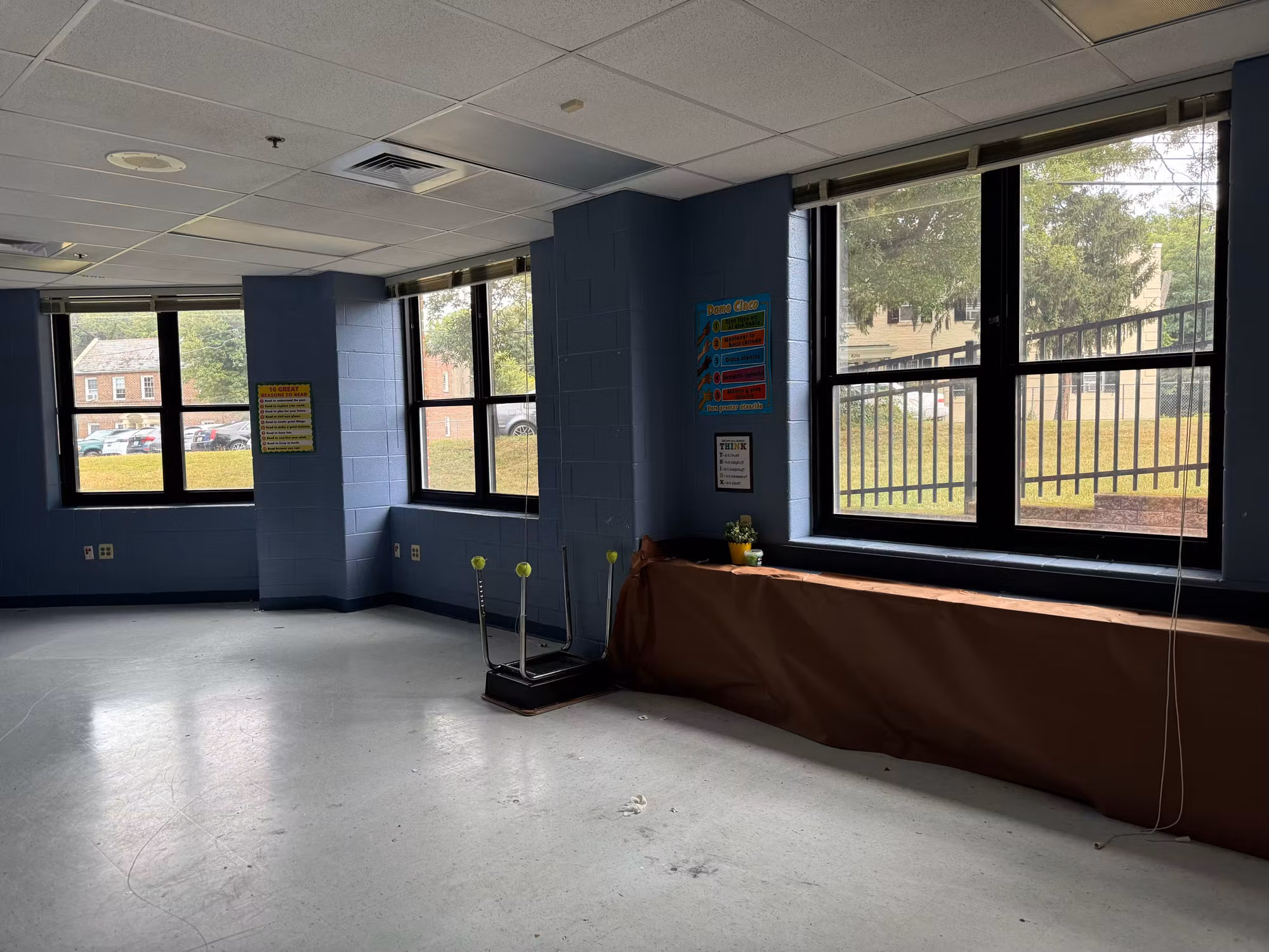 School classroom corner with large clear-glass windows overlooking a fenced grass field and blue block walls.