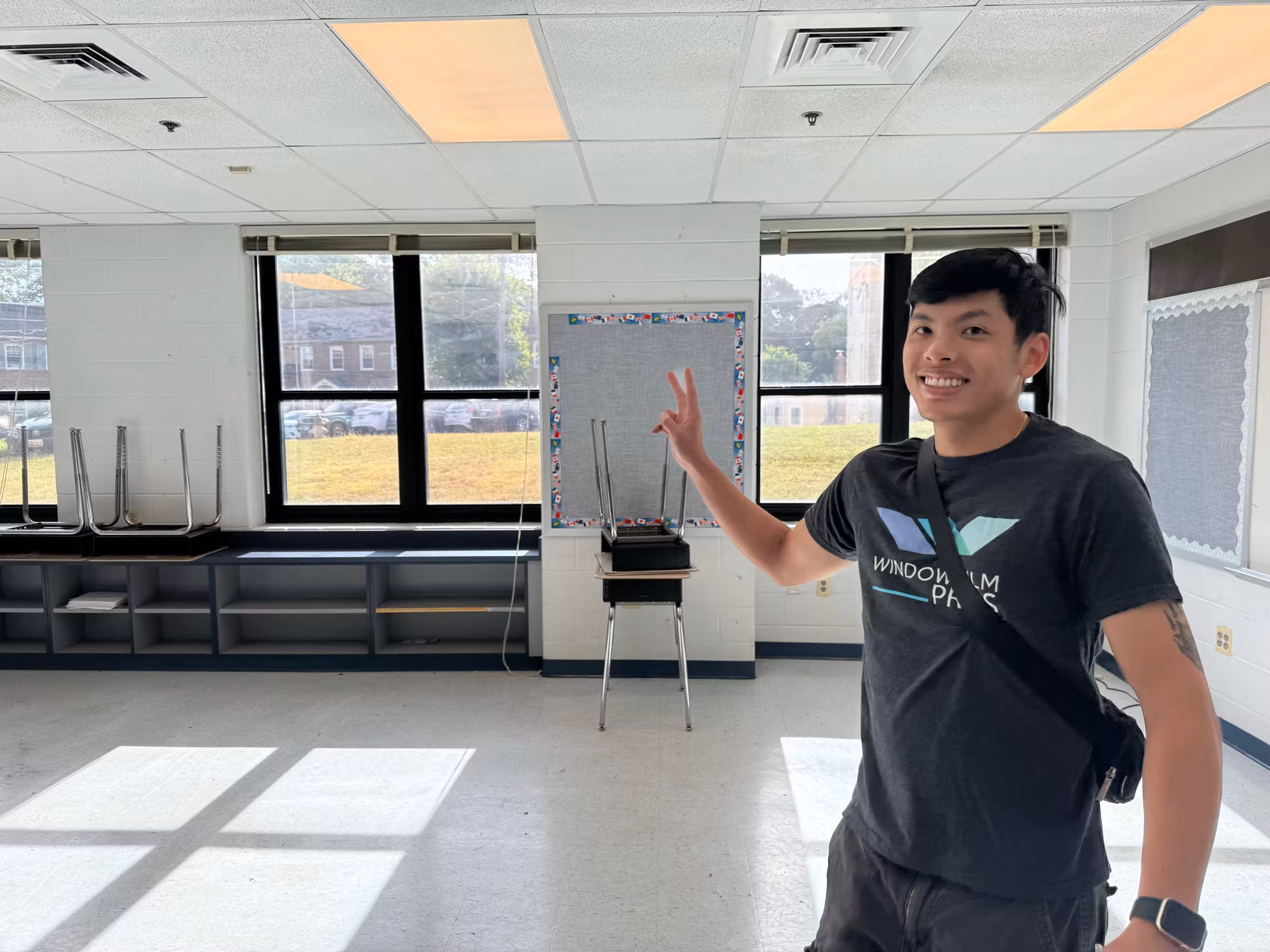 Installer gesturing toward classroom windows newly fitted with darkened solar control film.