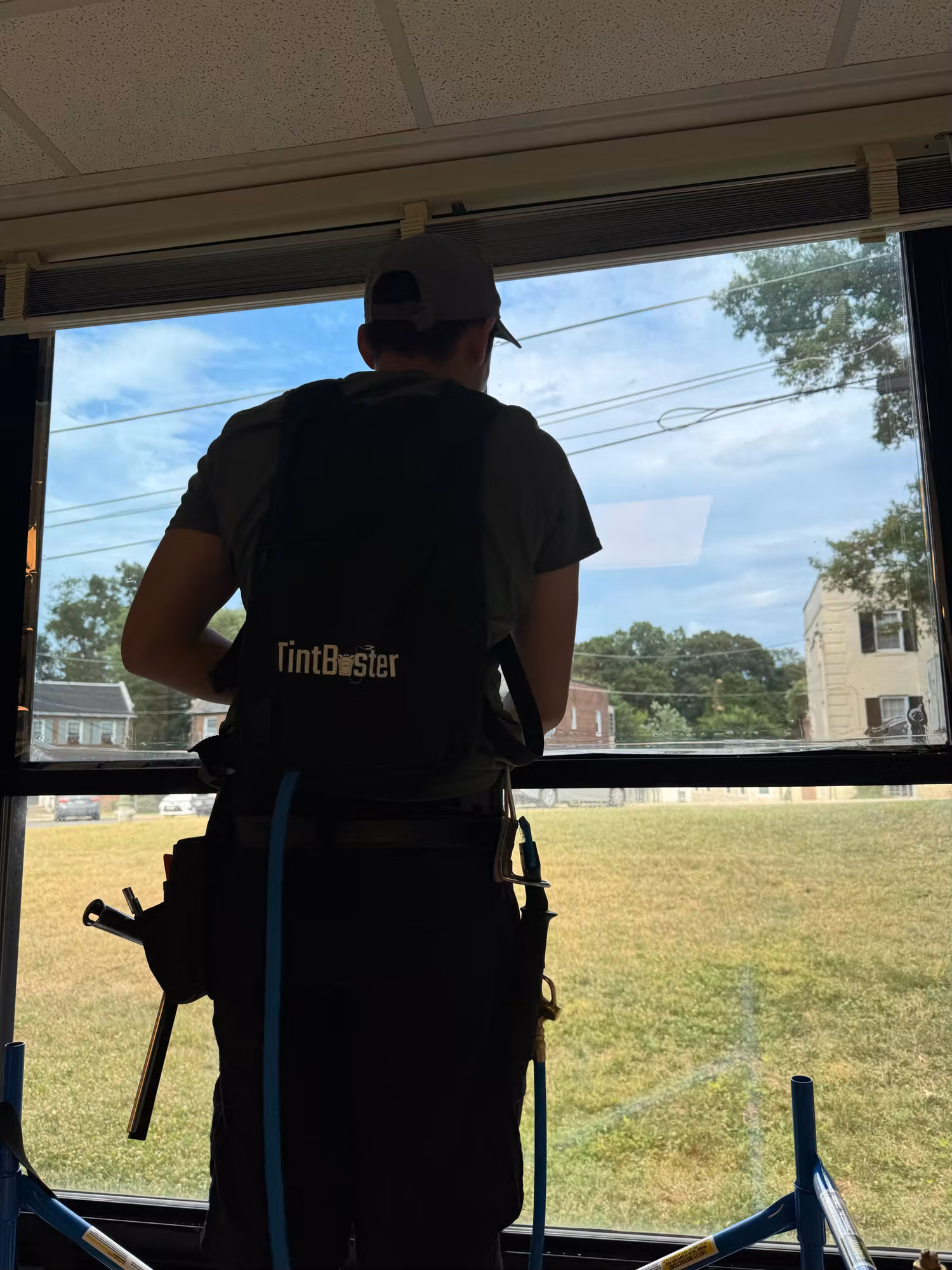 Installer applying darkening solar film to a large classroom window with a grass field visible outside.