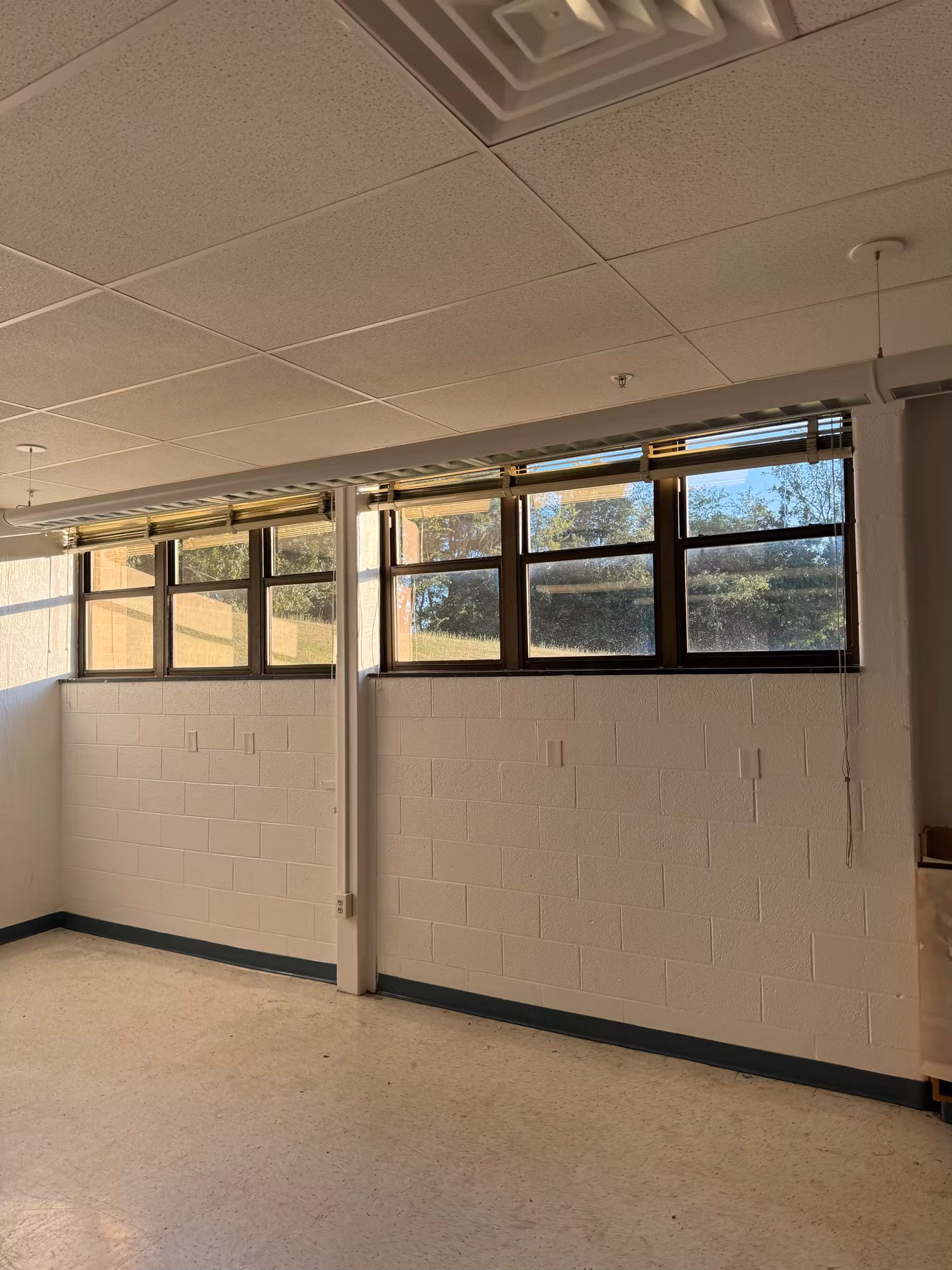 High clerestory windows above a white block wall in an empty school room letting in daylight.