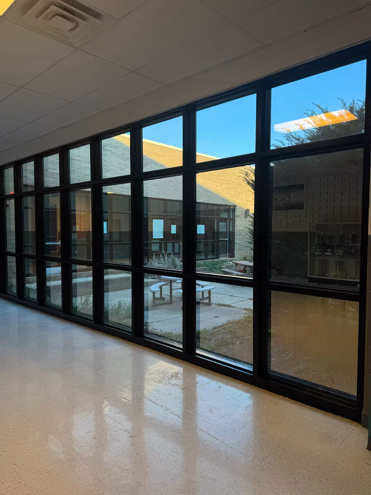 School hallway lined with floor-to-ceiling black-framed glass overlooking a brick courtyard with window film.