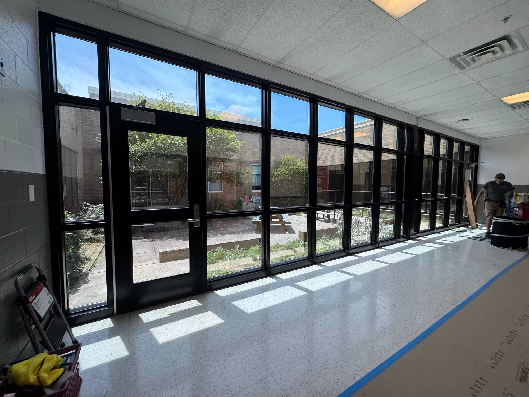 Floor-to-ceiling glazed wall with a door onto a courtyard, with floor masking and a worker present during film installation.