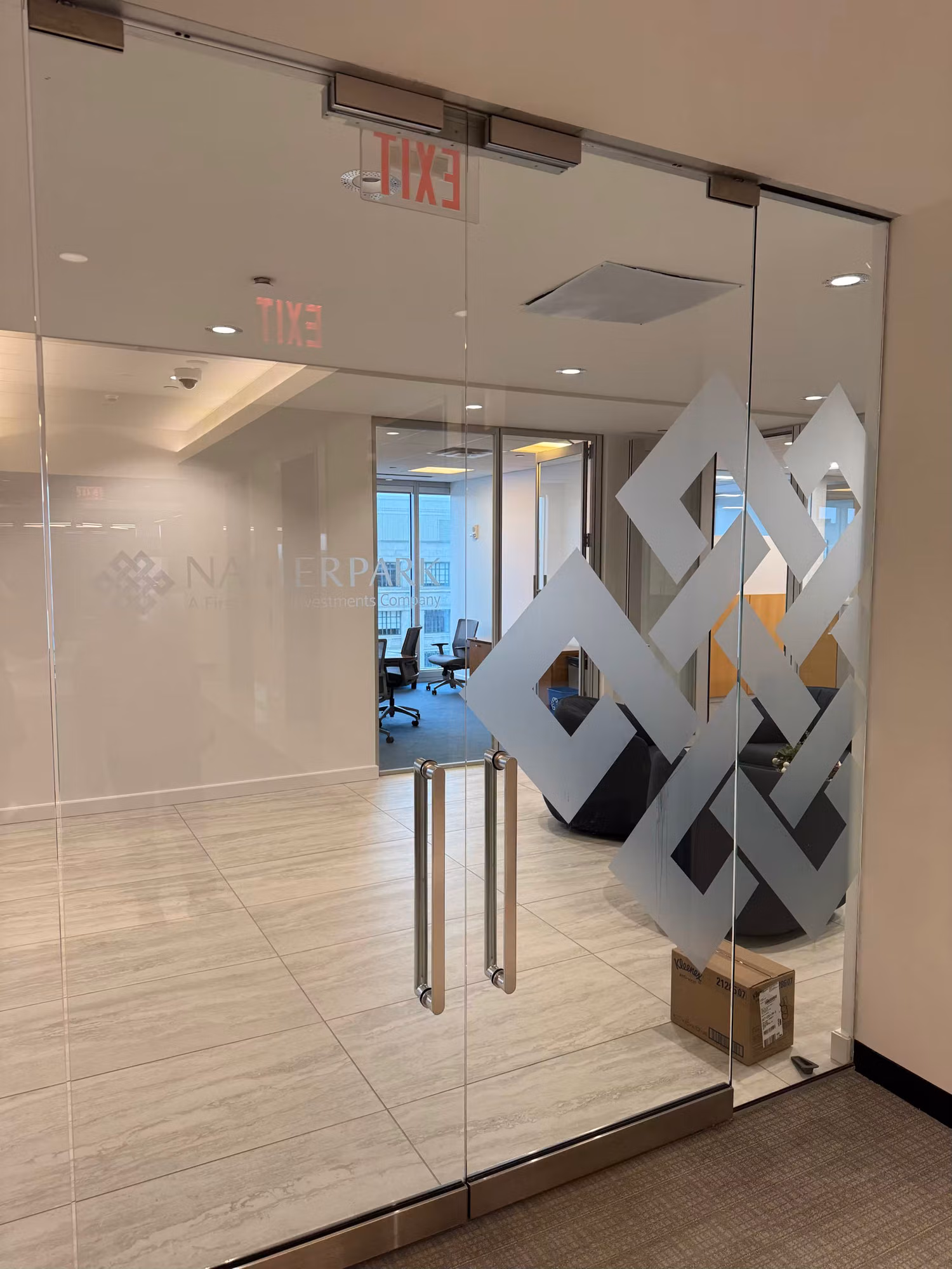 Frosted geometric logo graphic applied to glass office partition doors at a reception entry.