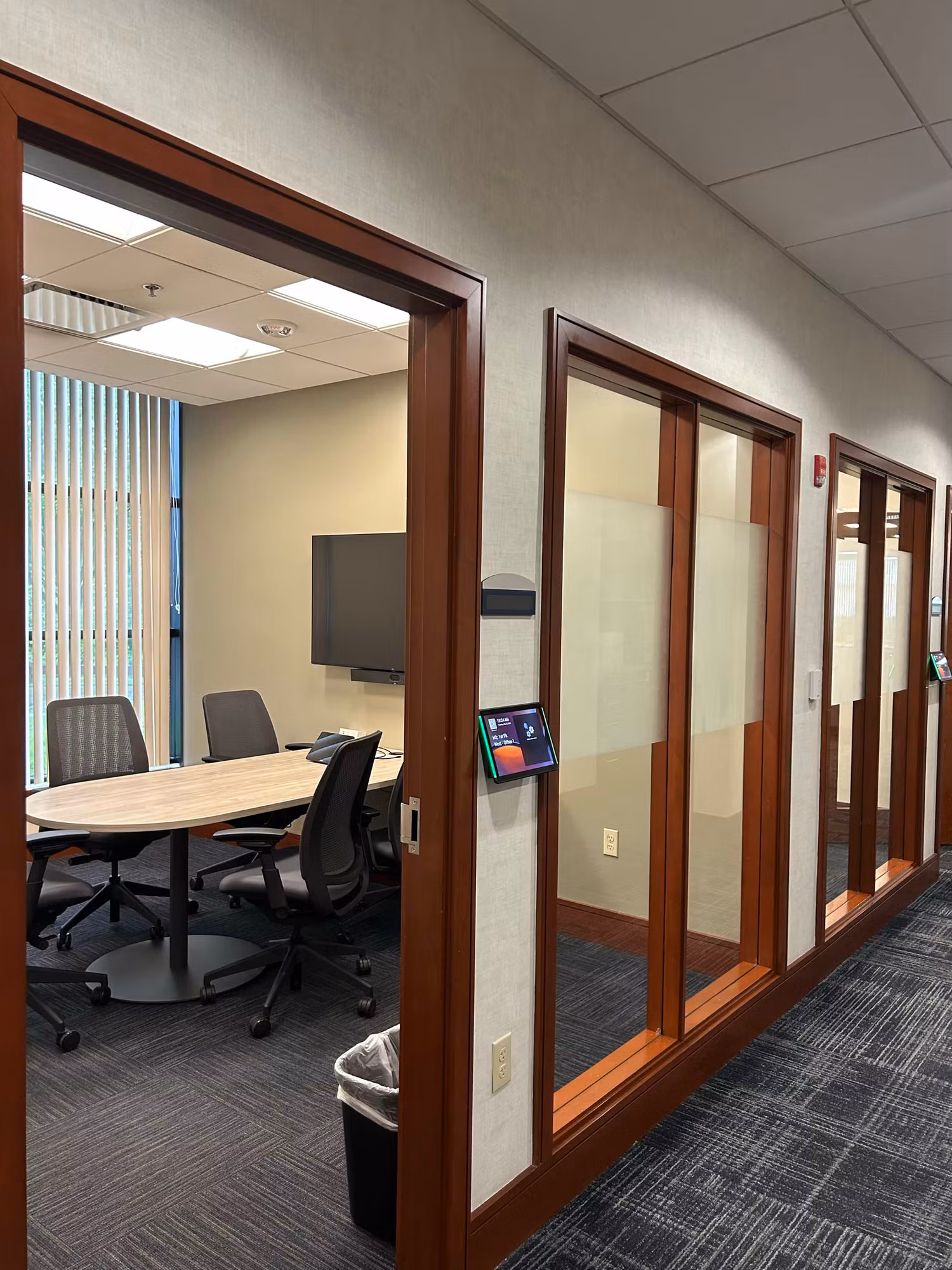 Conference room with table and monitor viewed through wood-framed glass doors with frosted privacy bands.
