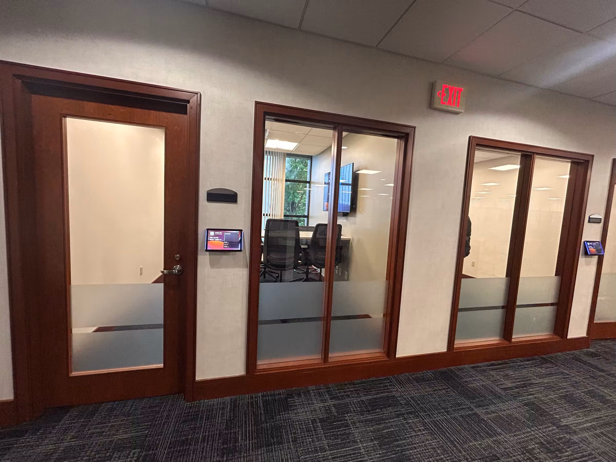 Office corridor lined with wood-framed conference room glass doors carrying lower frosted privacy bands.