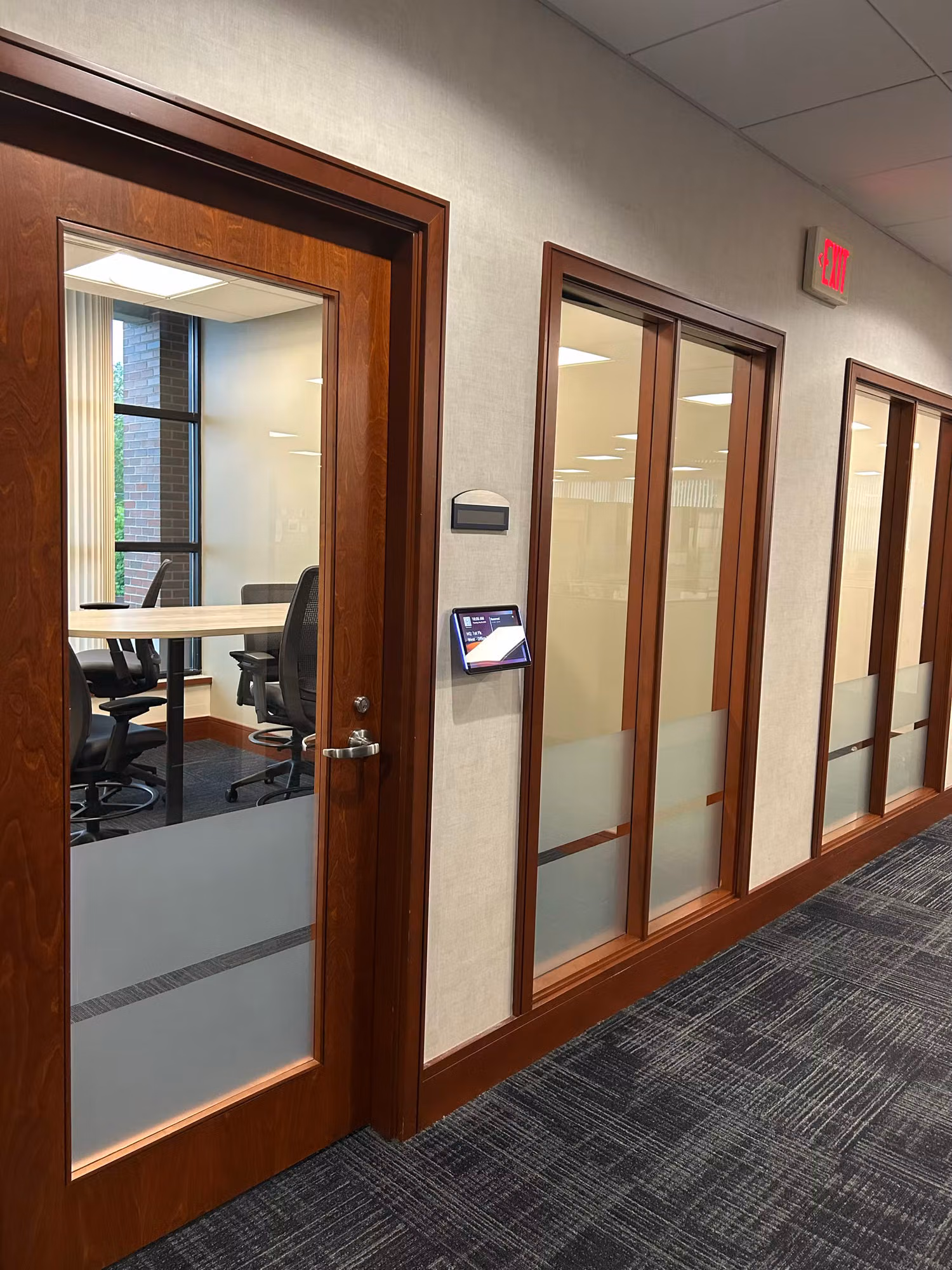 Hallway of wood-framed meeting room glass doors with frosted privacy bands across the lower glass.