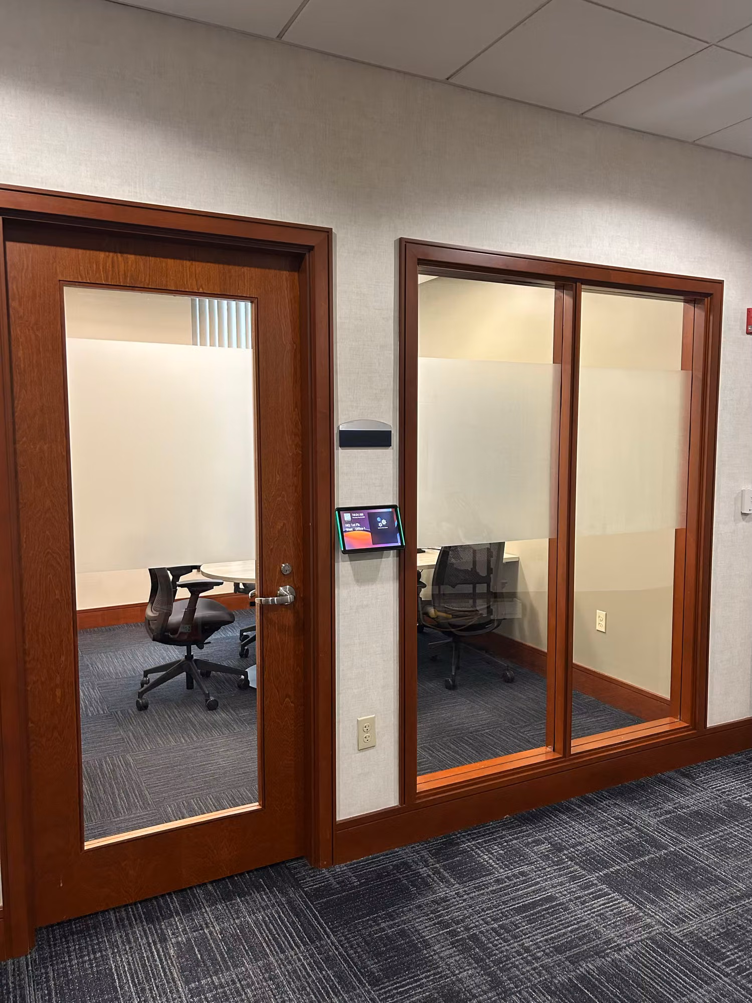 Two conference rooms behind wood-framed glass doors with frosted privacy banding on the lower panels.