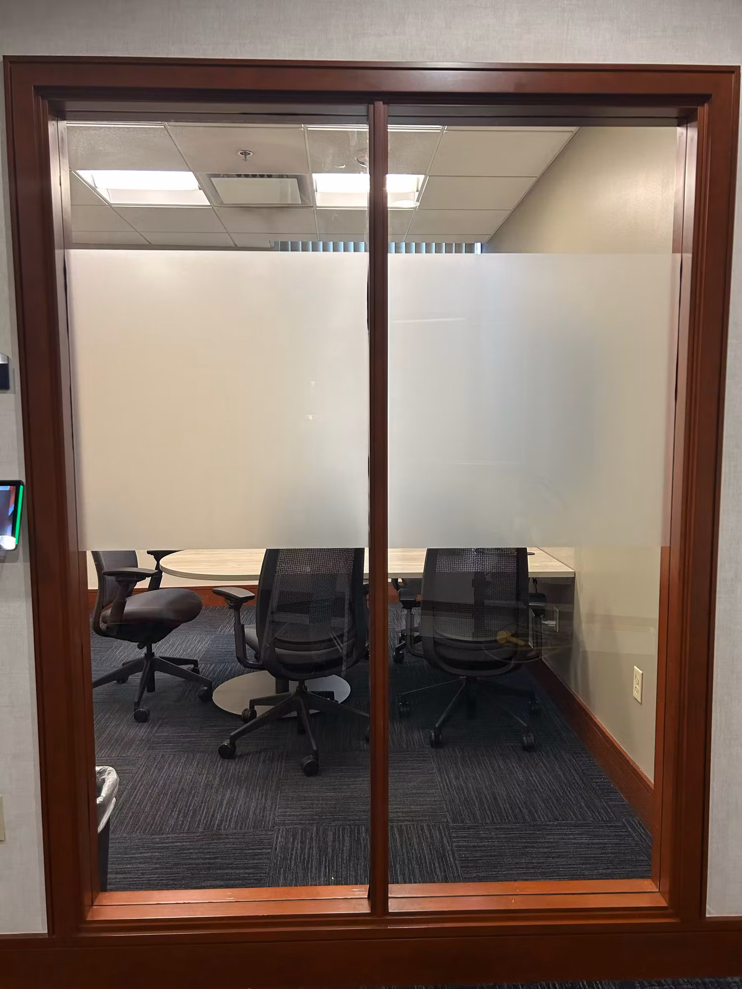 Wood-framed glass double doors with a frosted privacy band screening a conference room with chairs and a table.