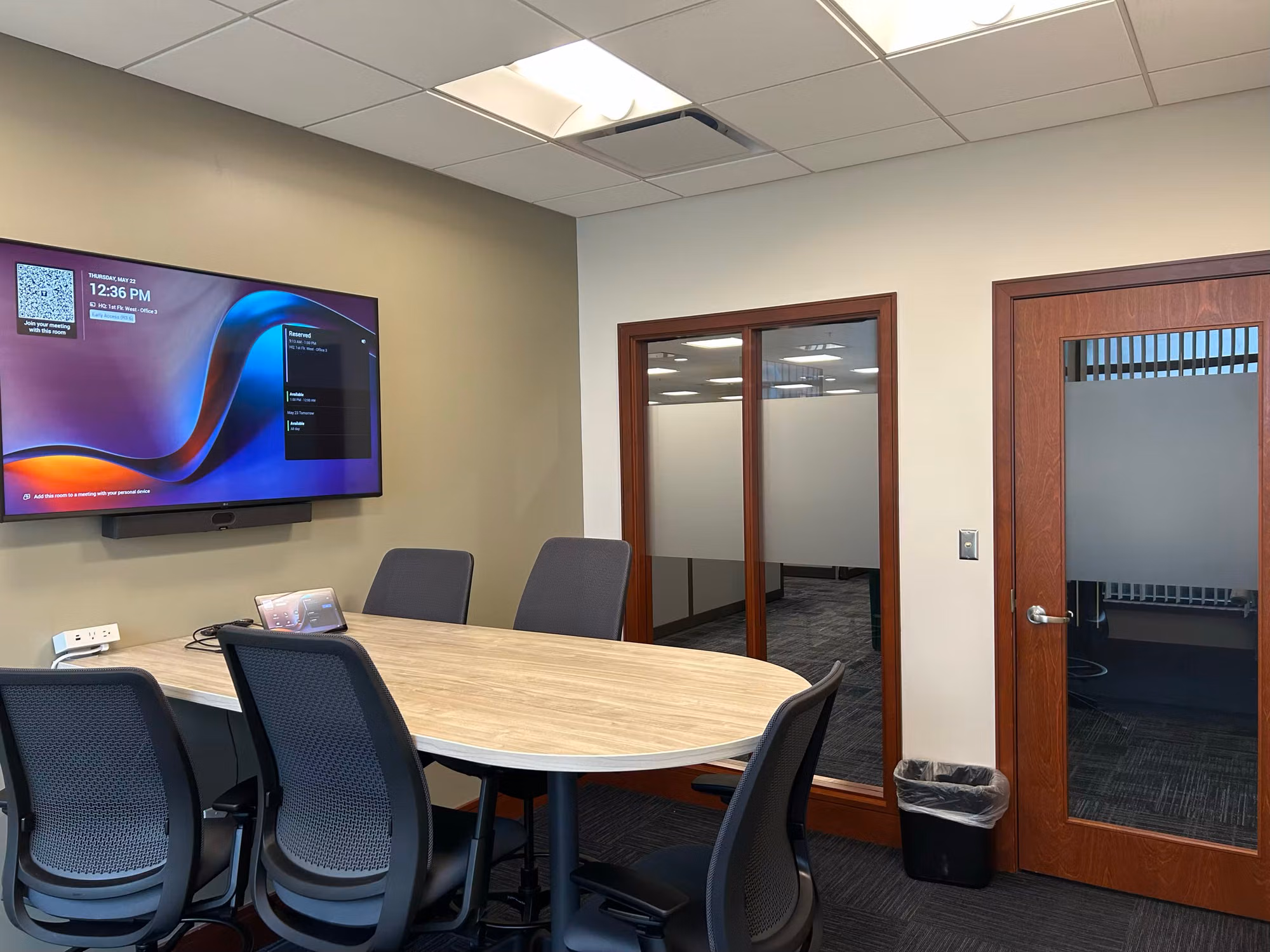 Meeting room with a mounted display, glass partition doors and a frosted glass door with privacy film alongside.