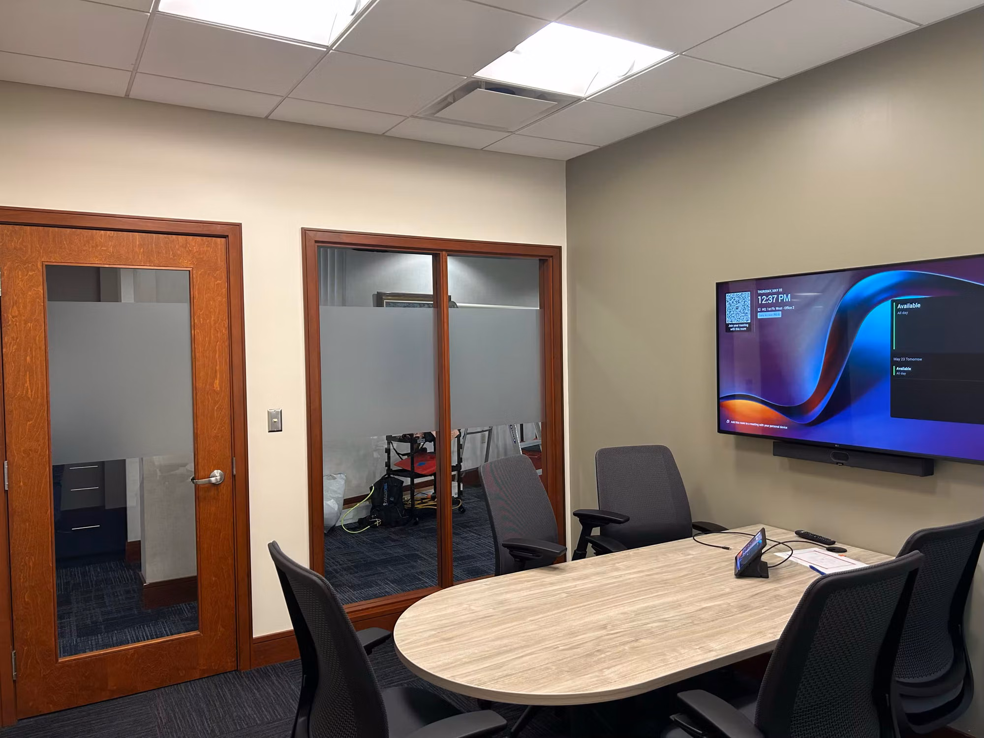Small conference room with glass partition doors and a frosted glass office door fitted with privacy film nearby.