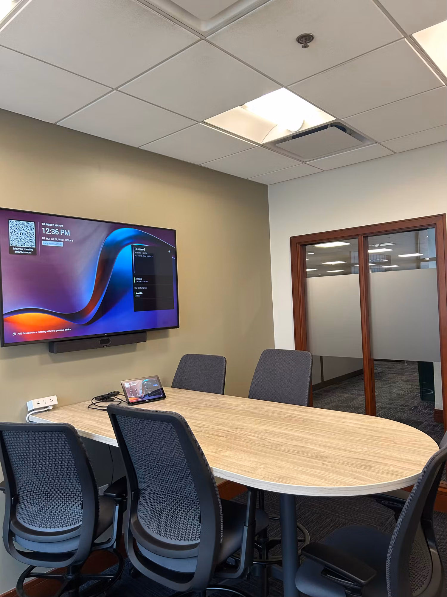 Conference room with a wall display and a glass partition wall fitted with a frosted privacy band for adjoining rooms.