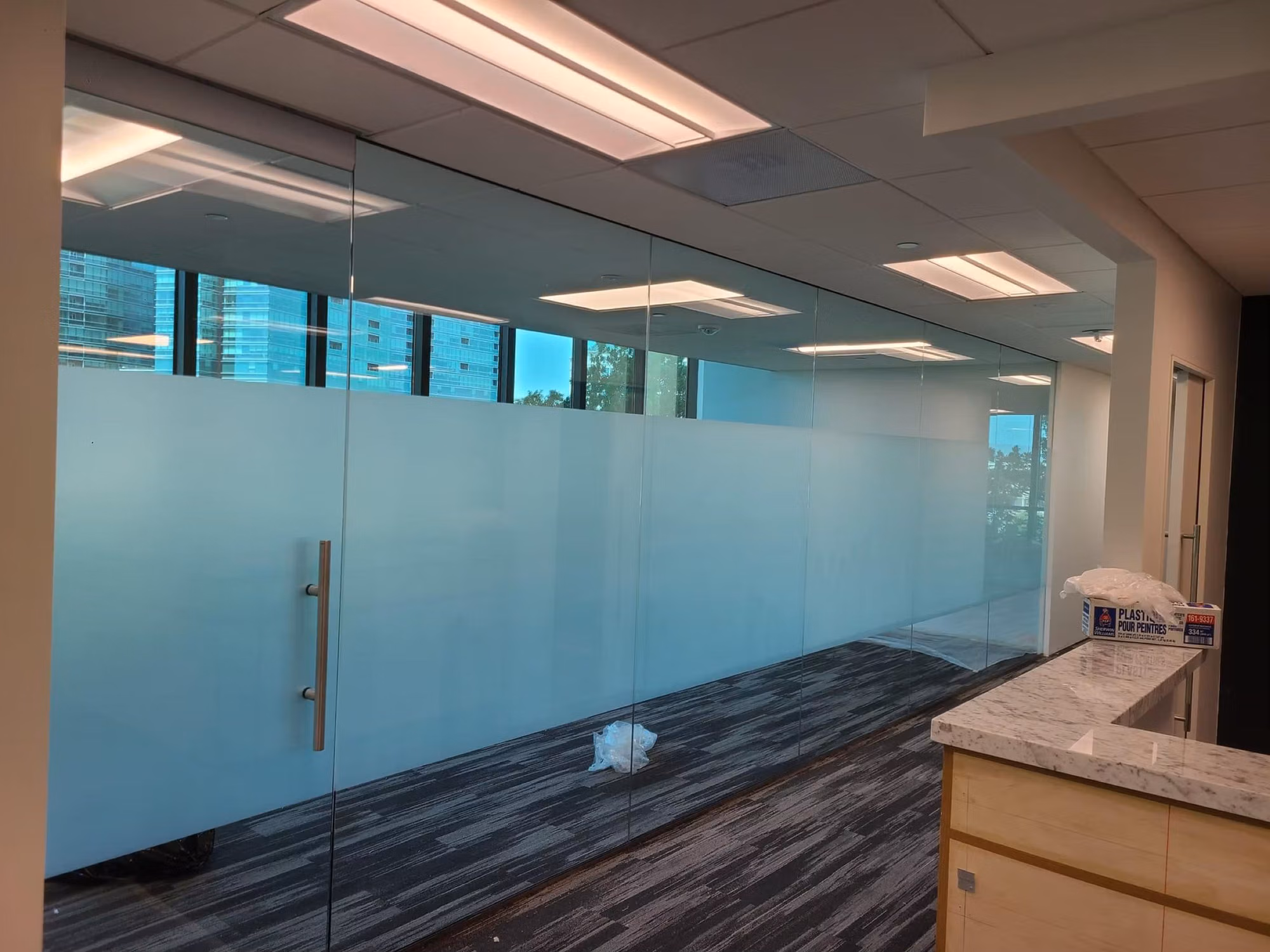 Floor-to-ceiling frameless glass office partition with a wide frosted privacy band and city view through the upper glass.