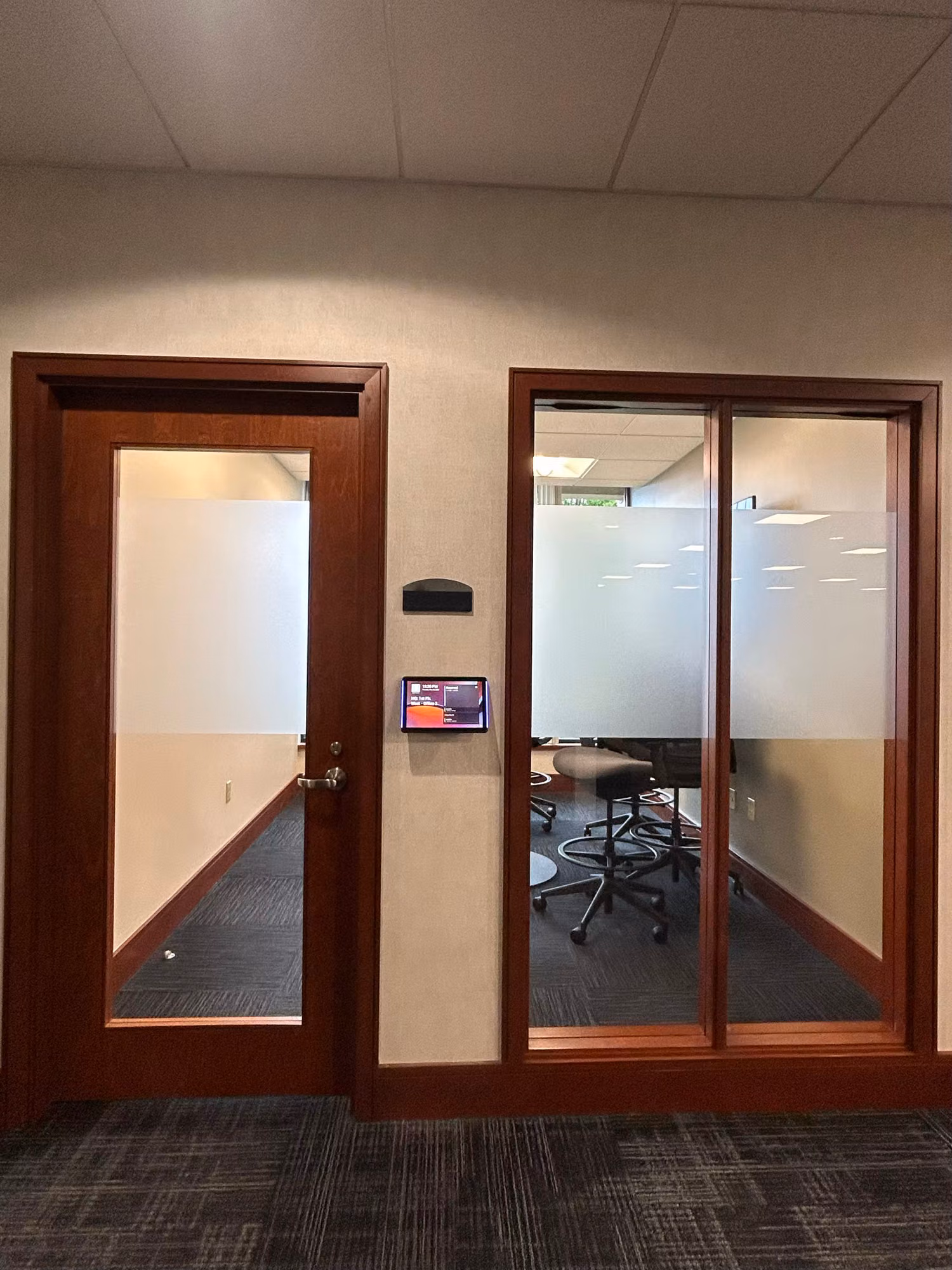 Frosted glass office door beside a glass partition with a privacy band leading into a small conference room.