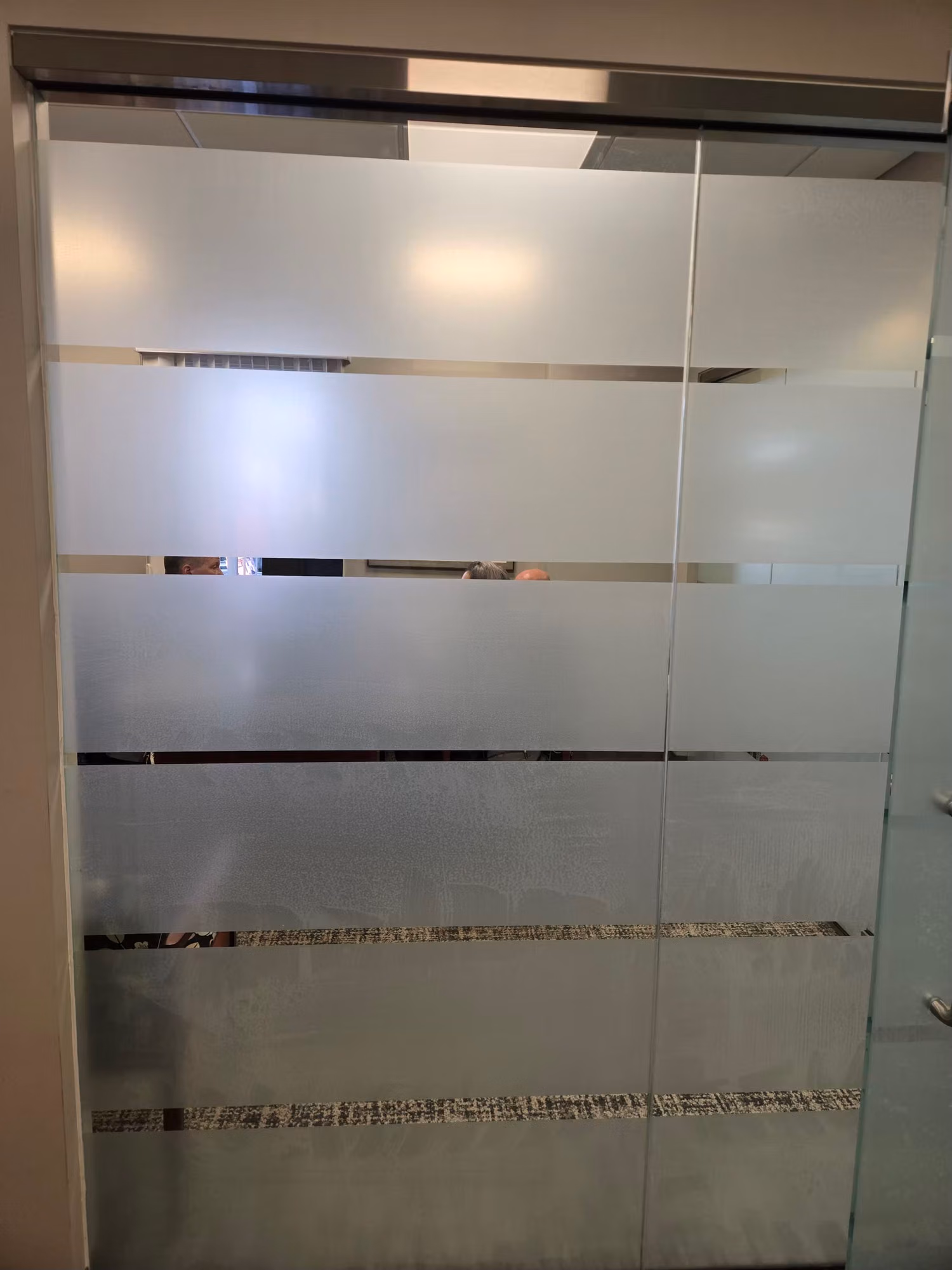 Close view of an office glass partition with horizontal frosted and clear striped privacy banding.