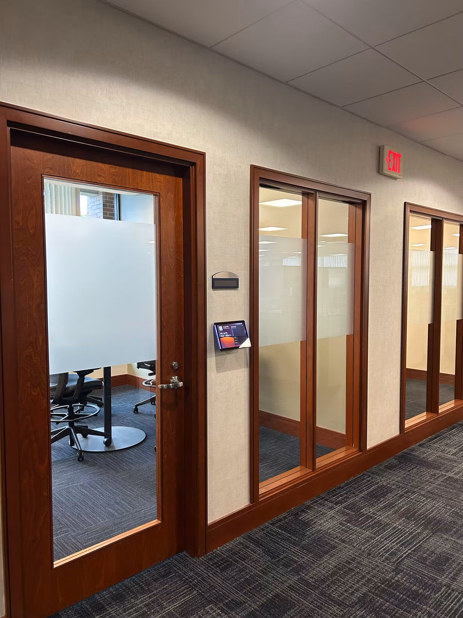Frosted glass office door and adjacent partition panels with privacy film along an interior corridor of meeting rooms.