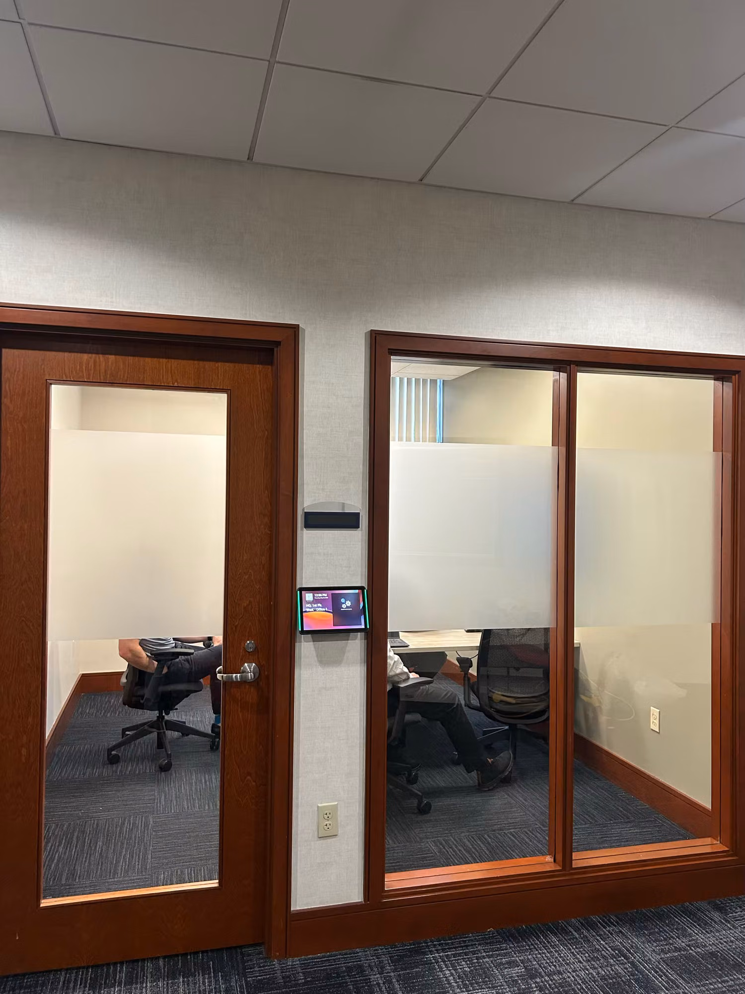 Wood-framed office glass doors and partition with frosted privacy film along the lower panels next to a conference room.