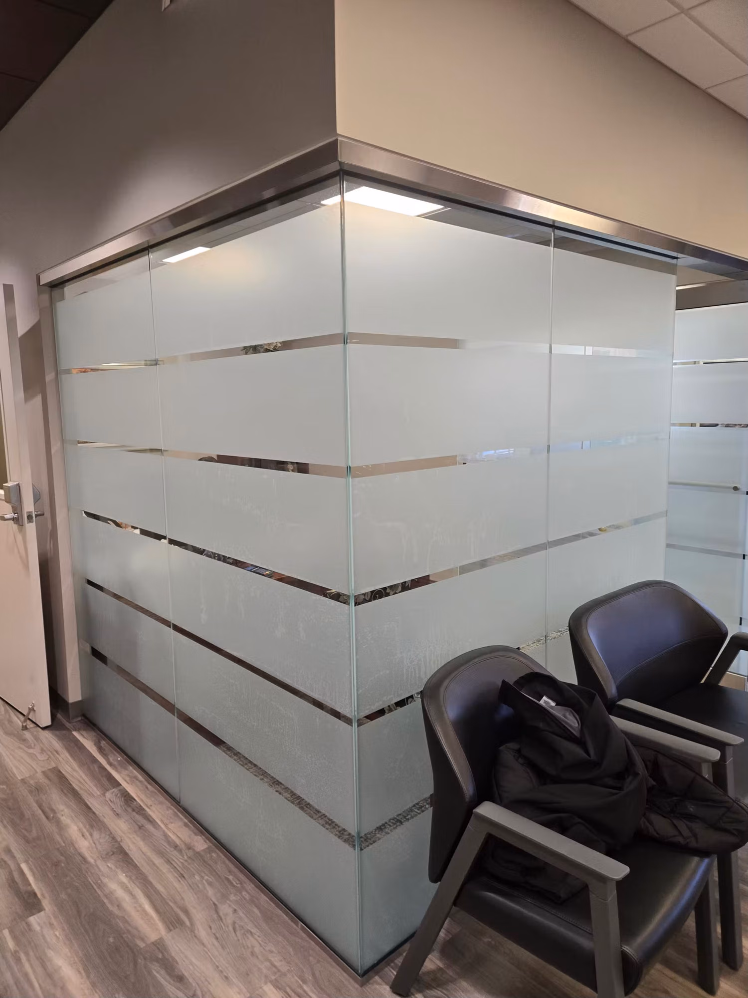 Corner office glass partition wall finished with alternating frosted and clear horizontal privacy bands.
