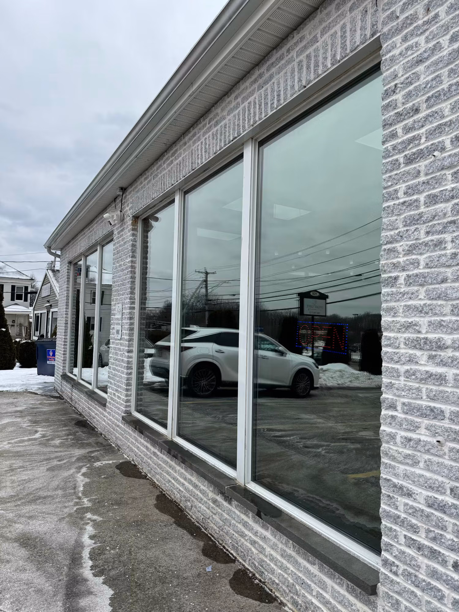 Row of large storefront windows on a brick commercial building with darkened solar control film reflecting the parking lot.