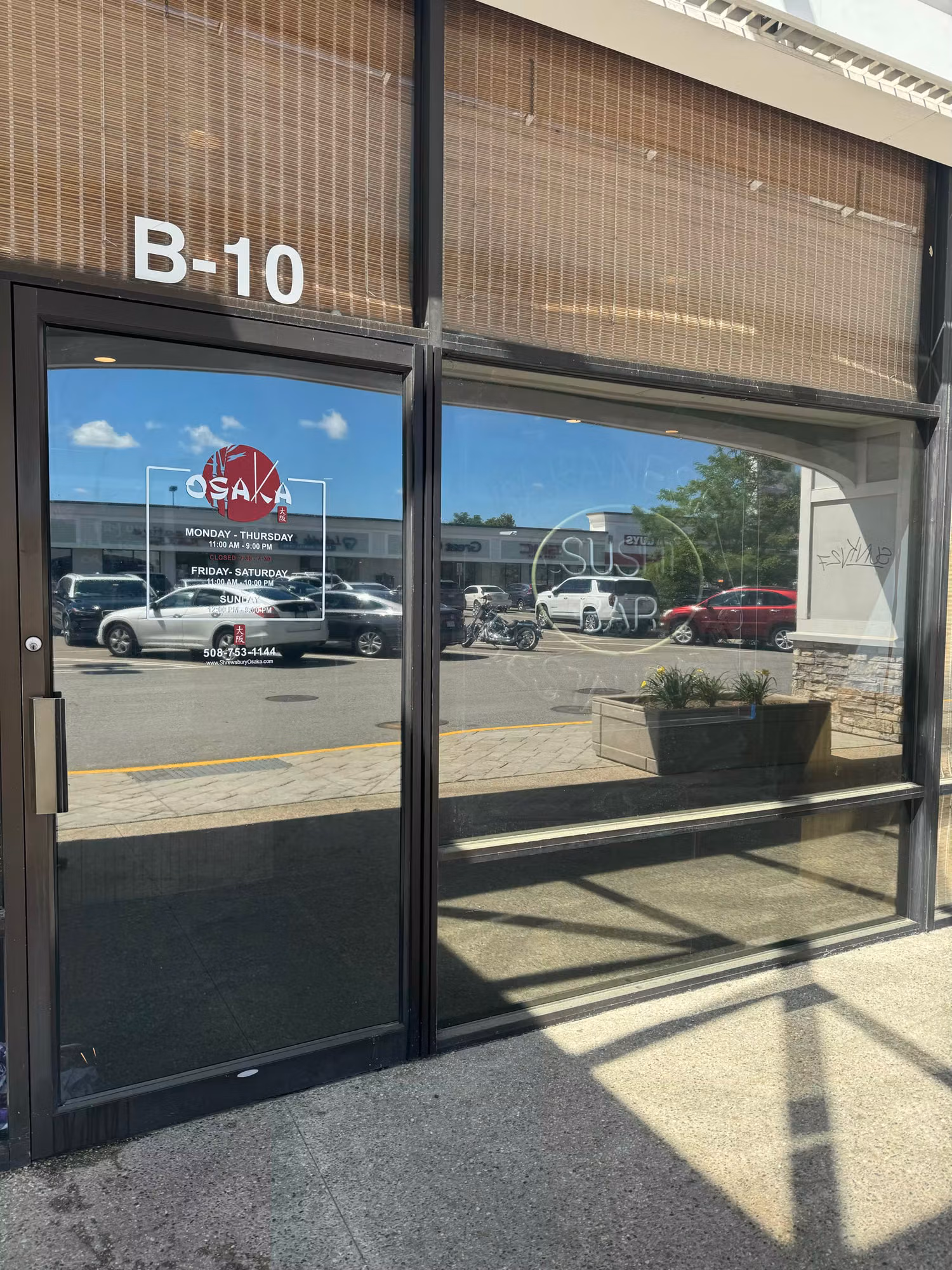 Glass storefront entry door with cut vinyl logo, business hours, and lettering applied to the window.