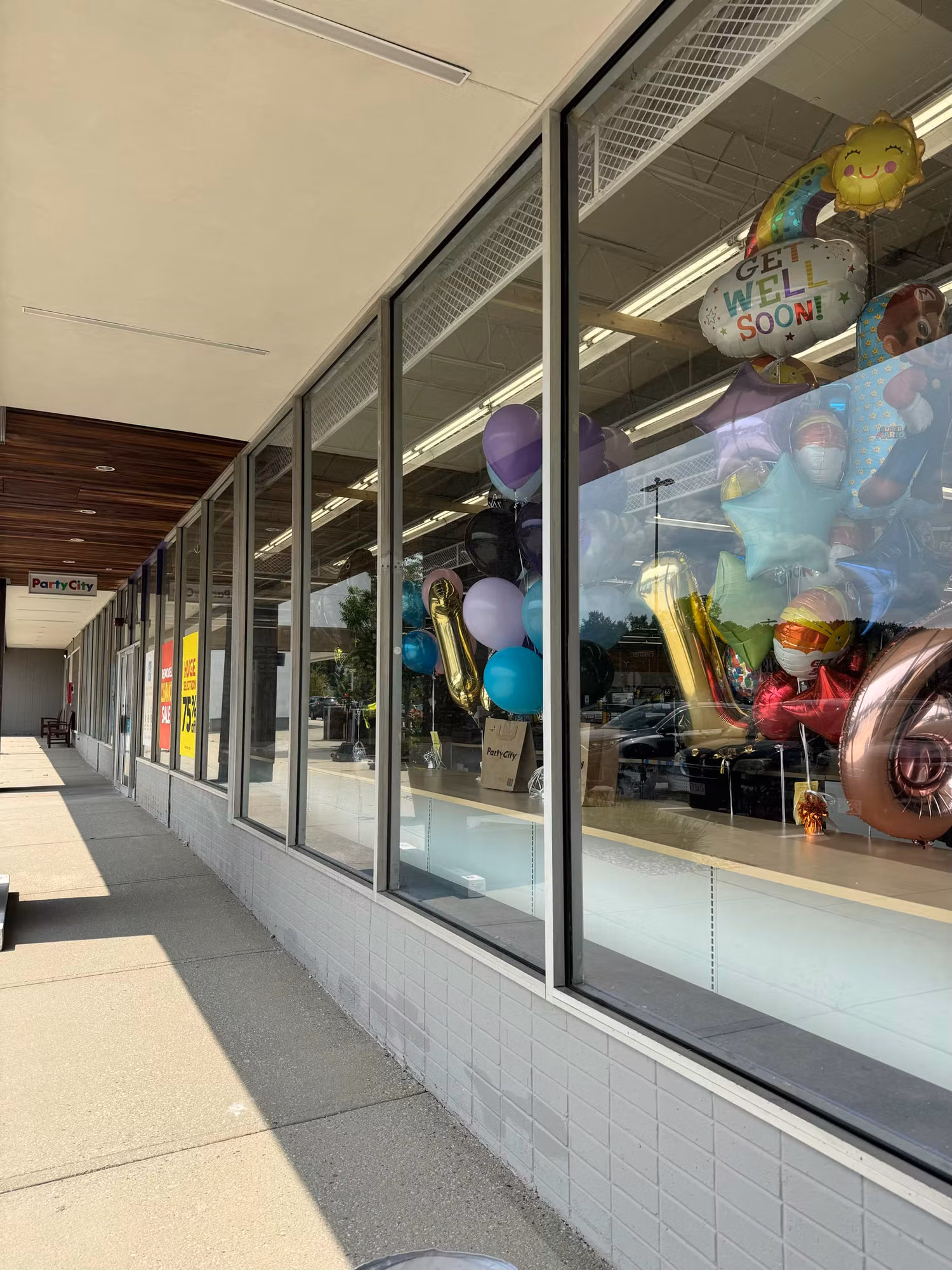 Retail storefront windows with darkened lower glass panels and party balloons displayed inside along the sidewalk.