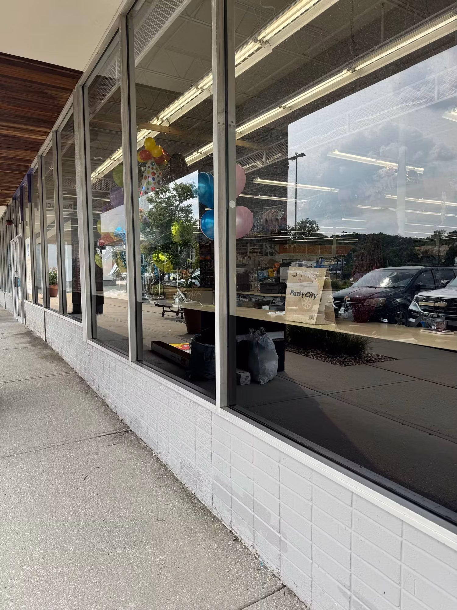 Retail storefront with tinted lower window panels reflecting parked cars and sky above a white brick wall.