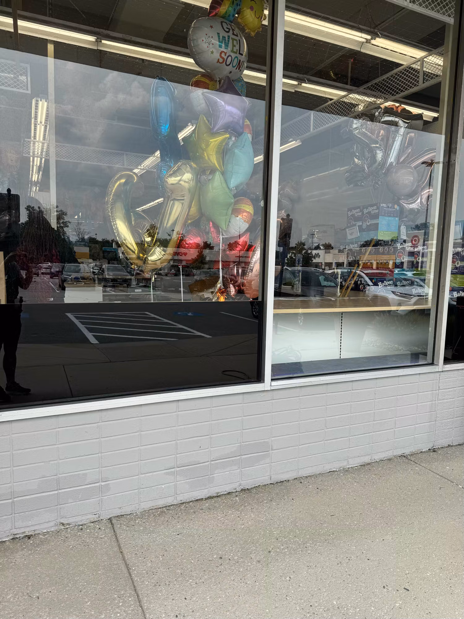 Corner storefront windows with tinted lower panels reflecting the parking lot and balloons behind the glass.