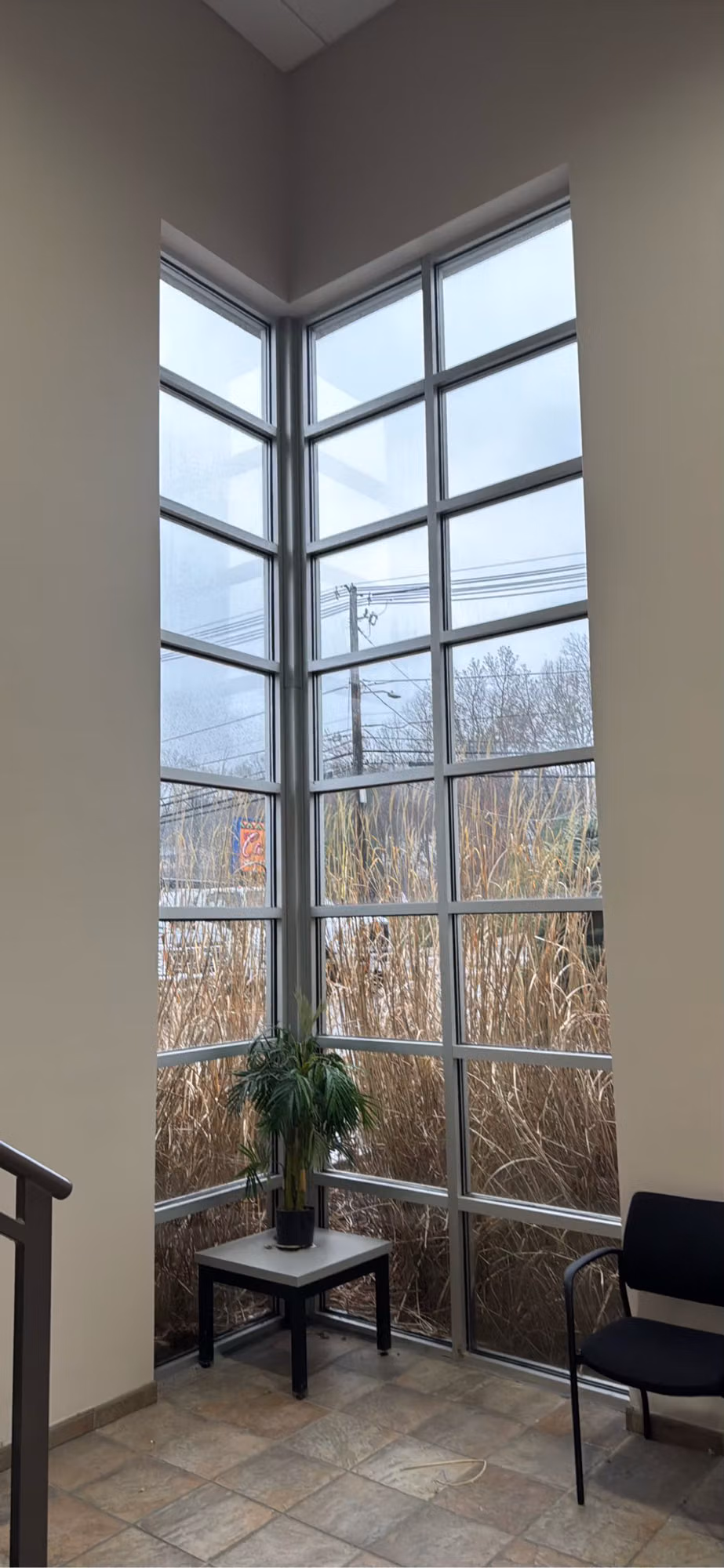Tall multi-pane atrium window with a white grid frame above a small lobby seating area.