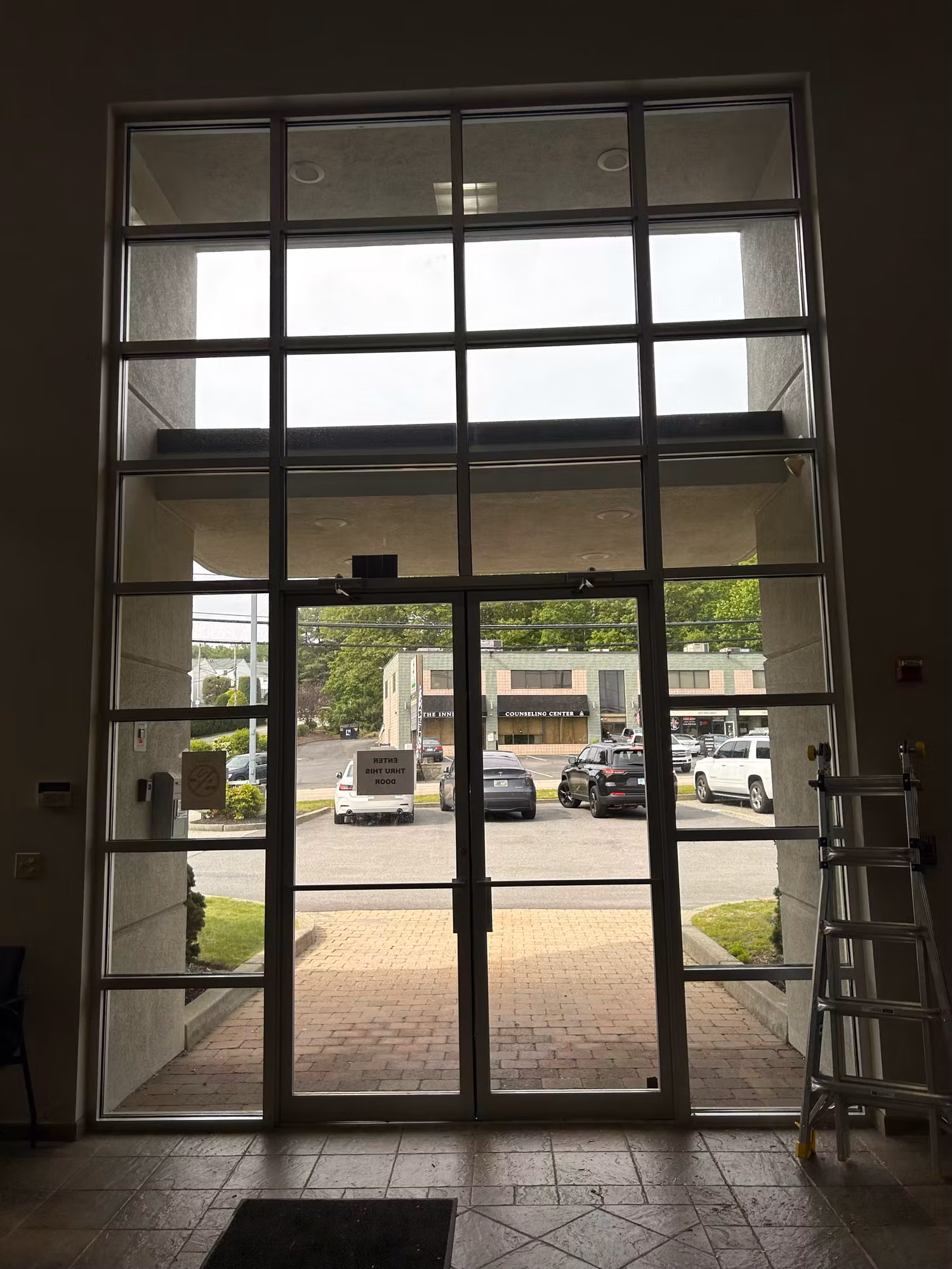 Two-story glass entry curtain wall and double doors with darkened solar film, viewed from a building lobby.