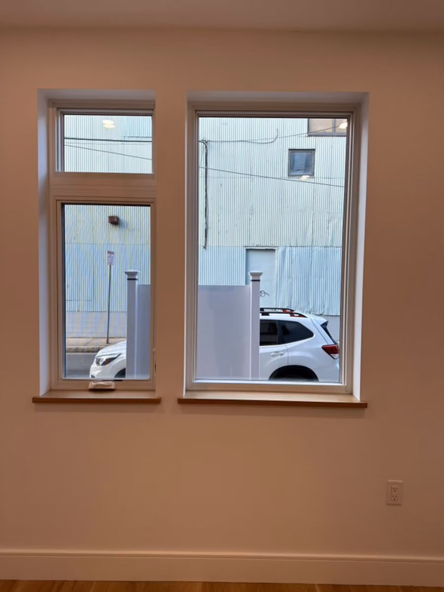 Two white-framed interior windows looking out to a parking area, glass treated with a clear protective film.
