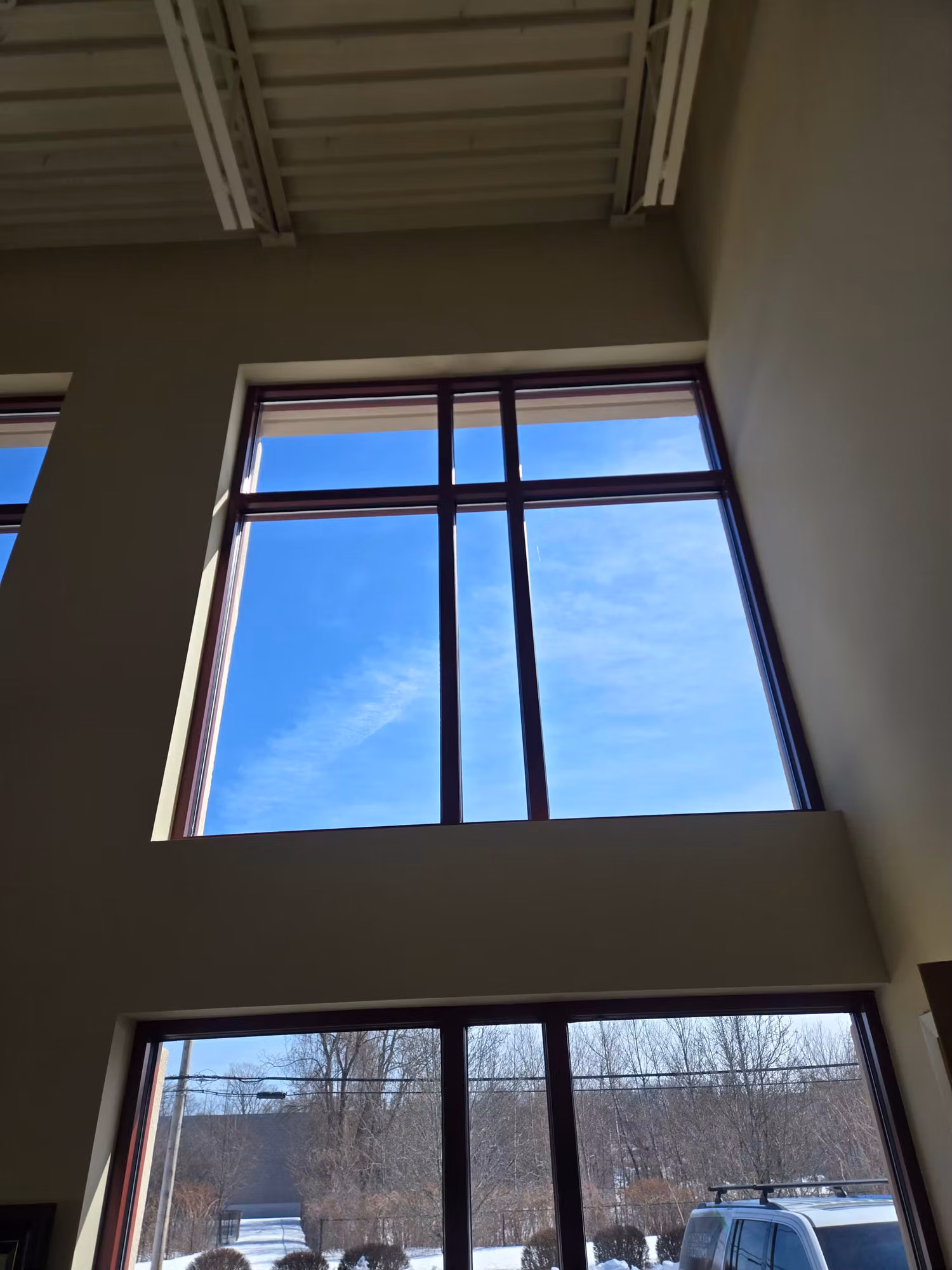 Tall two-story commercial lobby windows with tinted glass cutting glare while keeping a clear sky view.